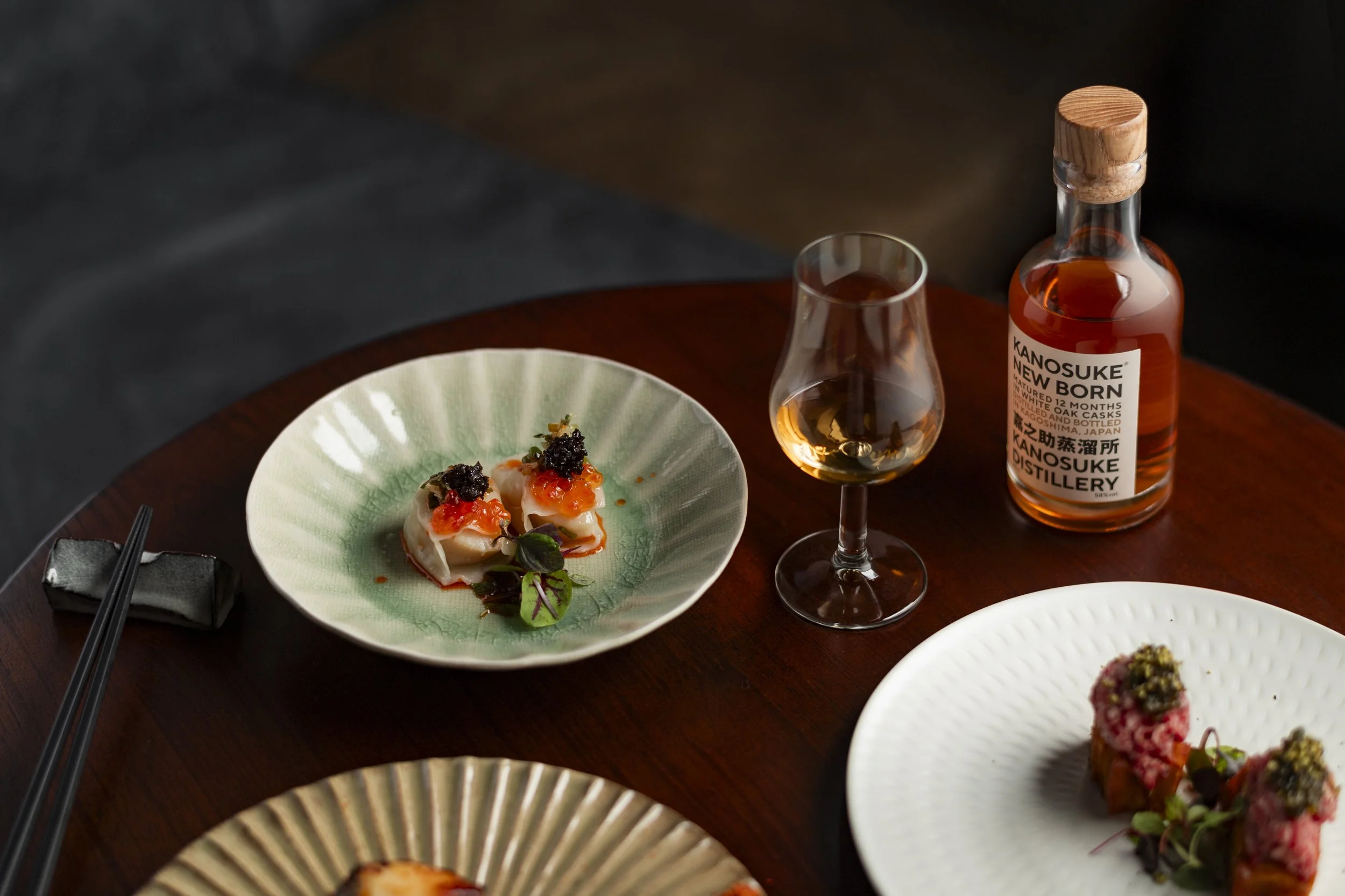 An elegant dining table with sushi, a glass of whiskey, and a bottle of Kanosuke whiskey at a restaurant.