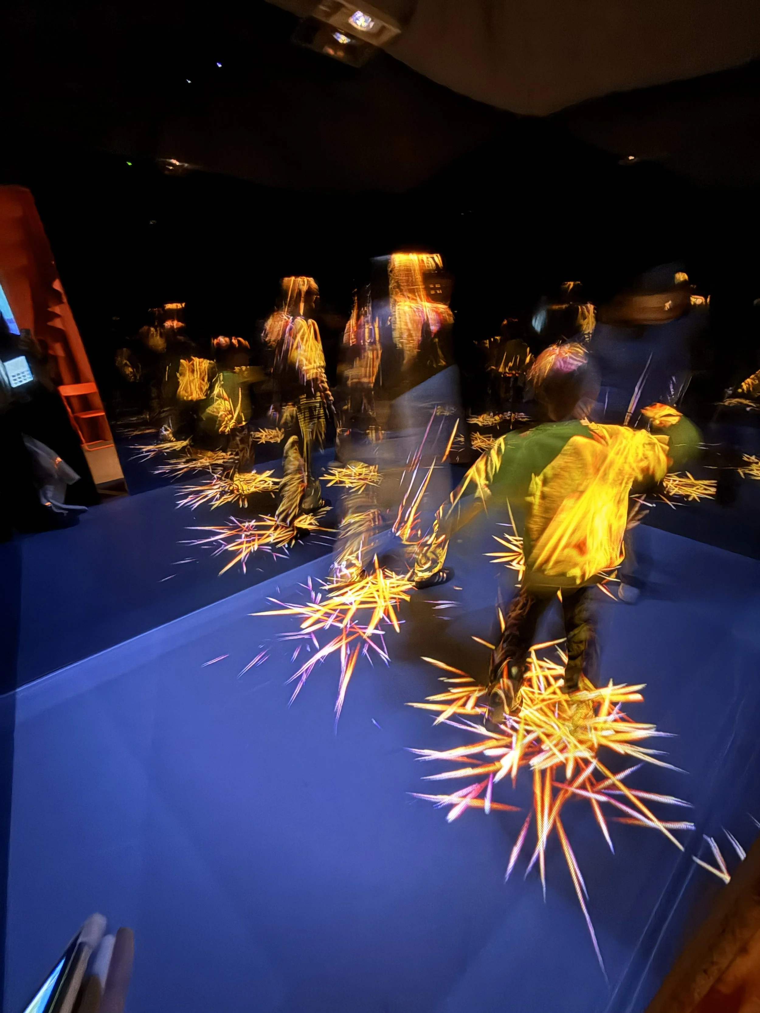 People playing with sparklers on a dark indoor floor, with the sparklers creating bright streaks of light.