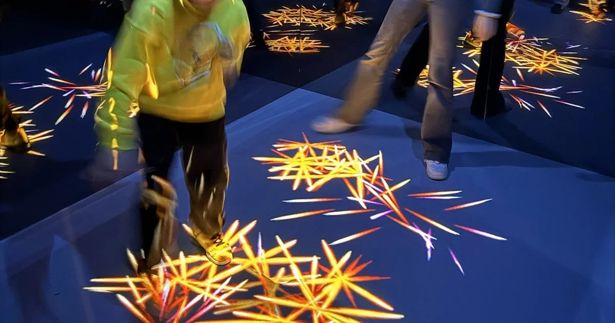 People walking on an interactive floor projection of colorful, glowing star-shaped patterns.