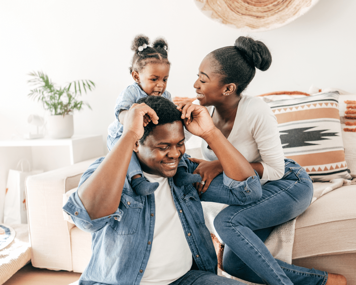 Happy family playing together in living room, woman, man, and young girl enjoying fun moment.