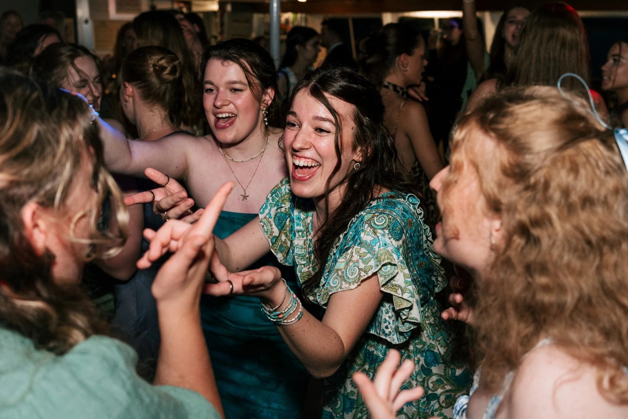 A group of young women laughing and dancing at a party or celebration, with one woman in a patterned dress as the focal point.