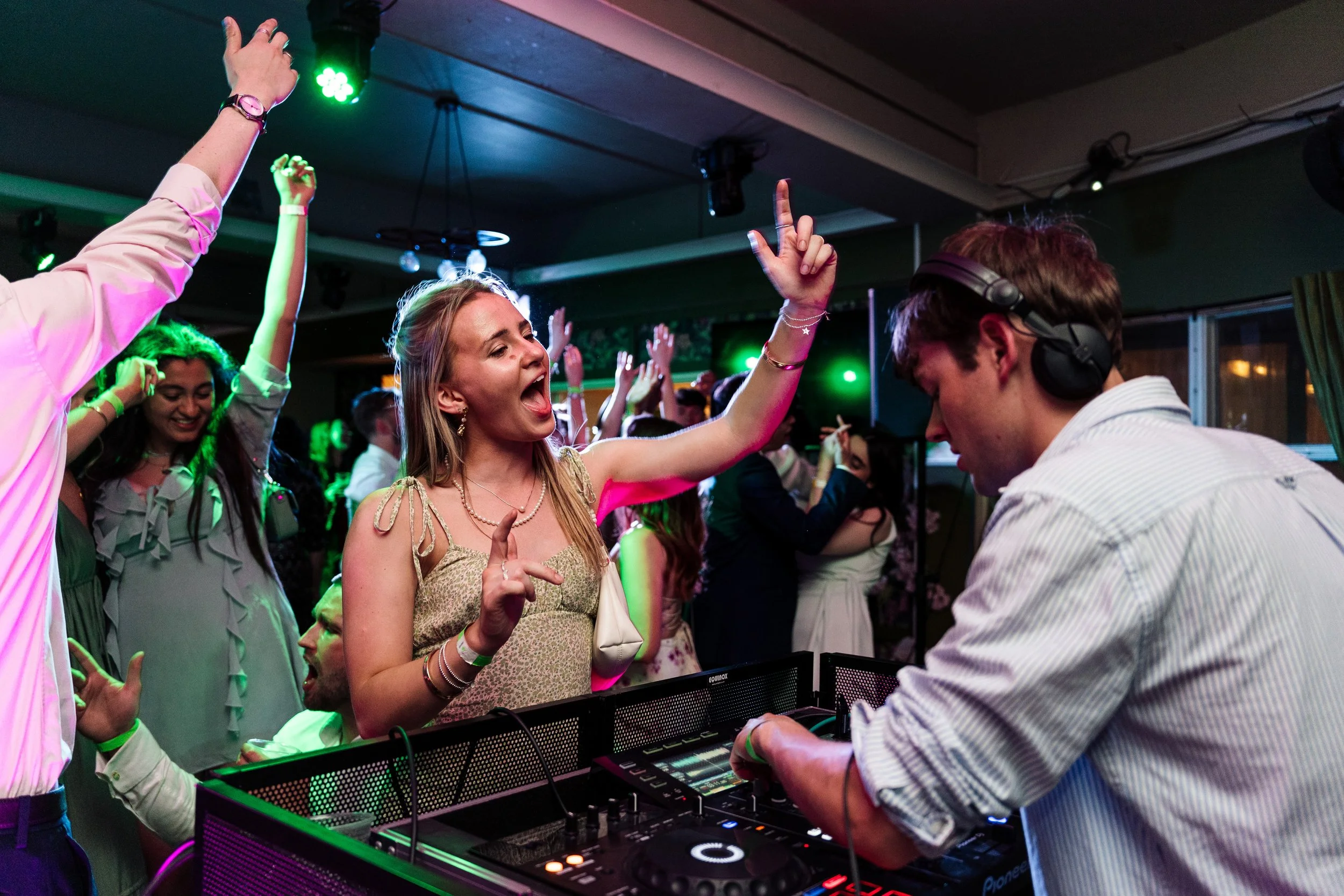 People dancing and enjoying music at a party with a DJ playing in front of them, colorful lighting, and a lively atmosphere.