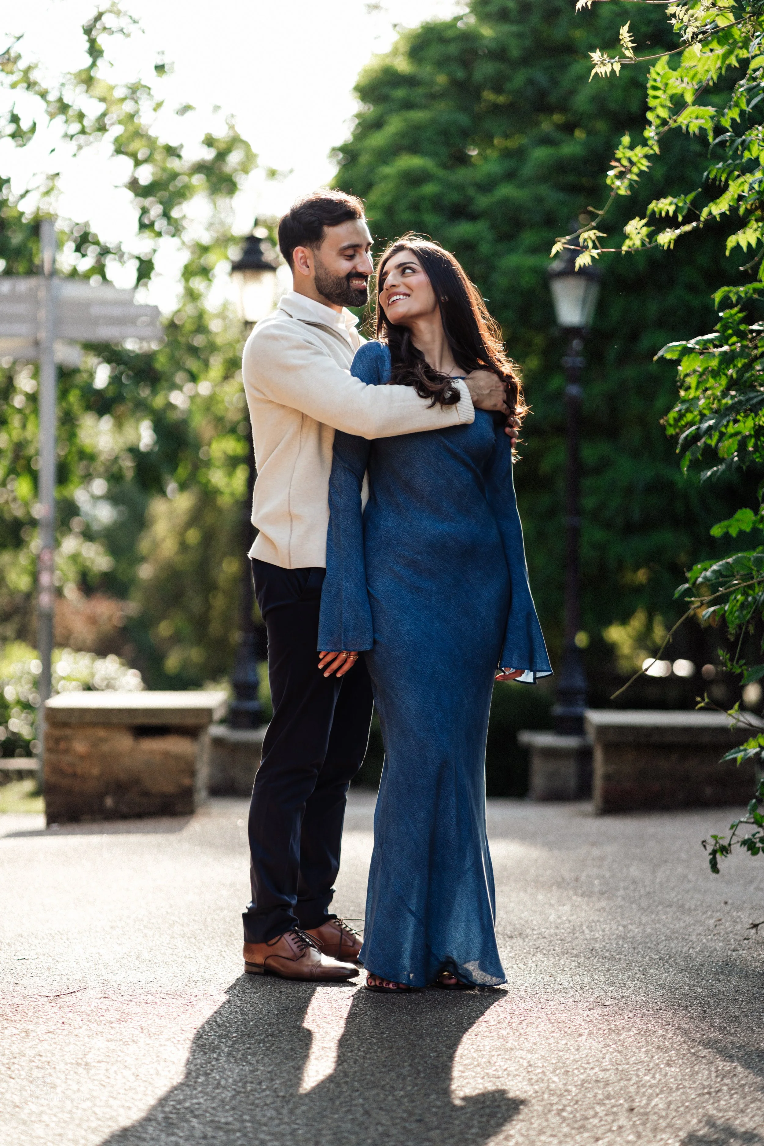 A couple standing close together outdoors in a park, smiling and looking at each other.
