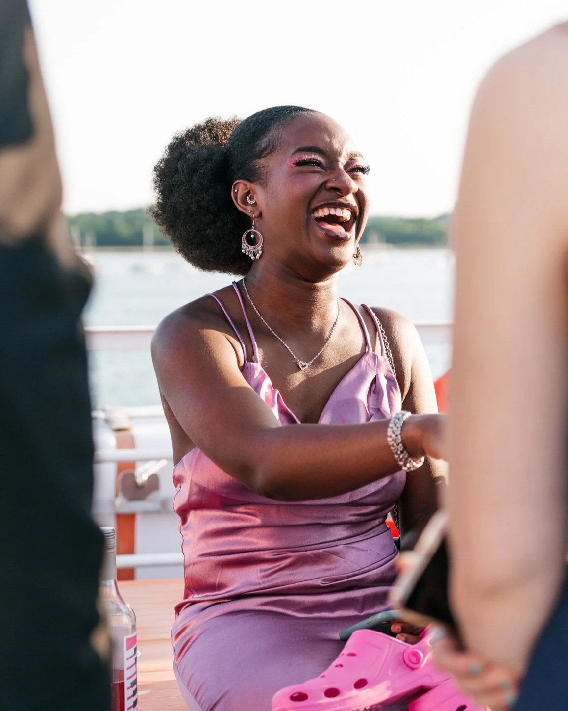 A woman in a purple dress laughing with a group of friends outdoors near water.
