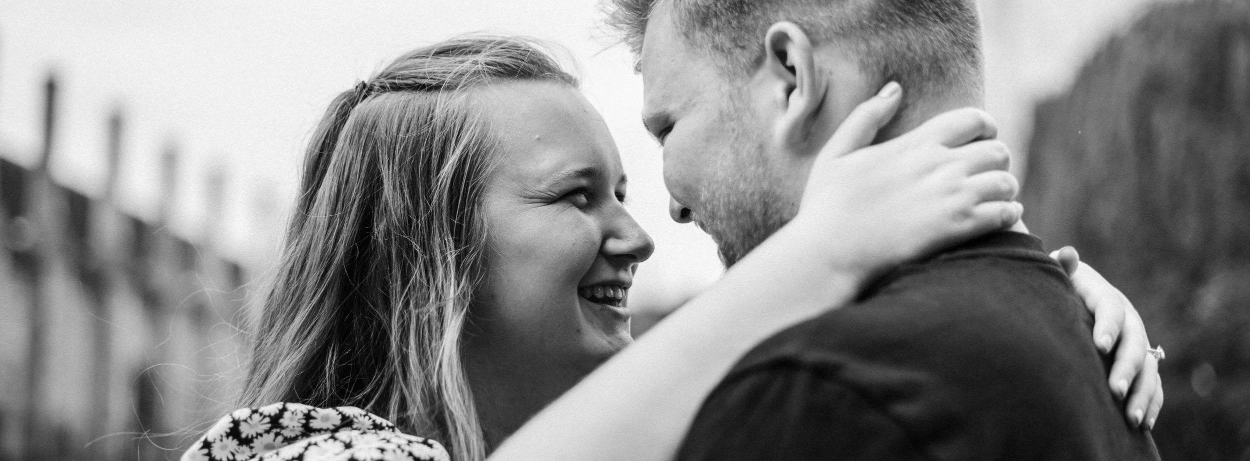 A young woman and a young man are close together, smiling and touching foreheads in a black and white photo.