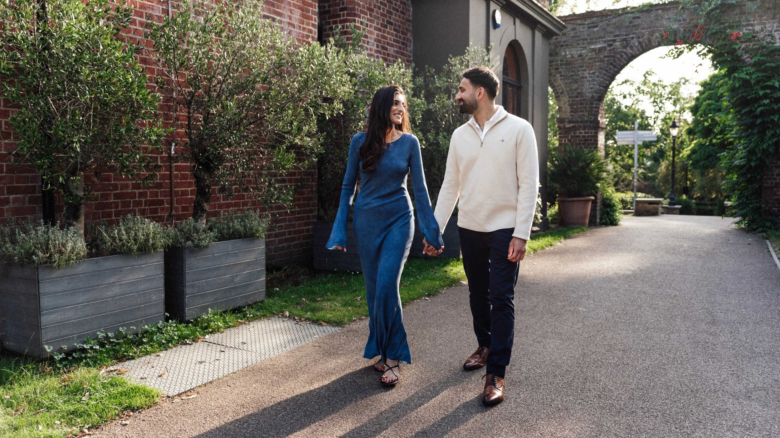 A couple walking hand in hand outdoors on a sunny day, smiling at each other and enjoying each other's company.