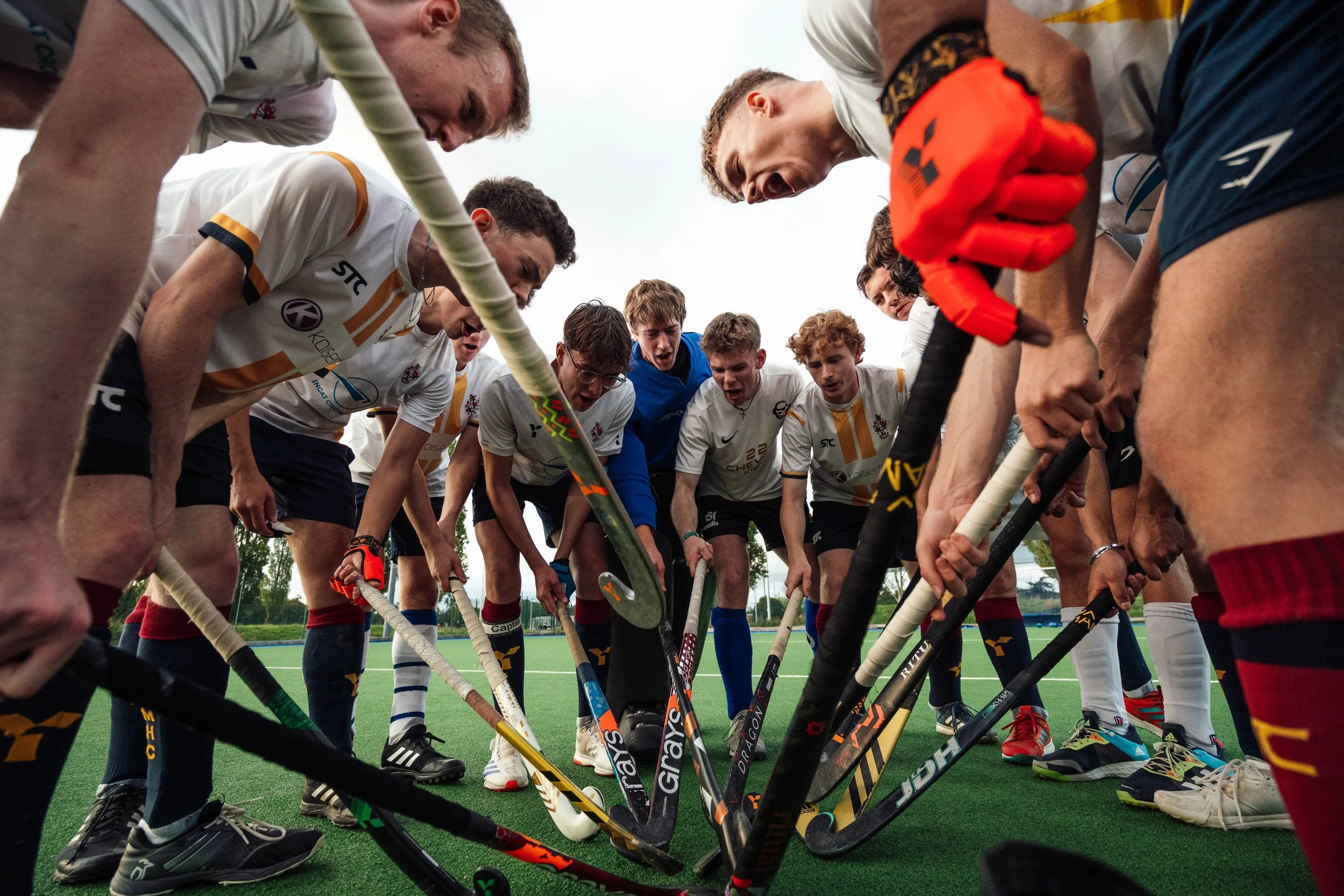 Hockey players in a huddle on a field, holding their sticks in the center, preparing for game.