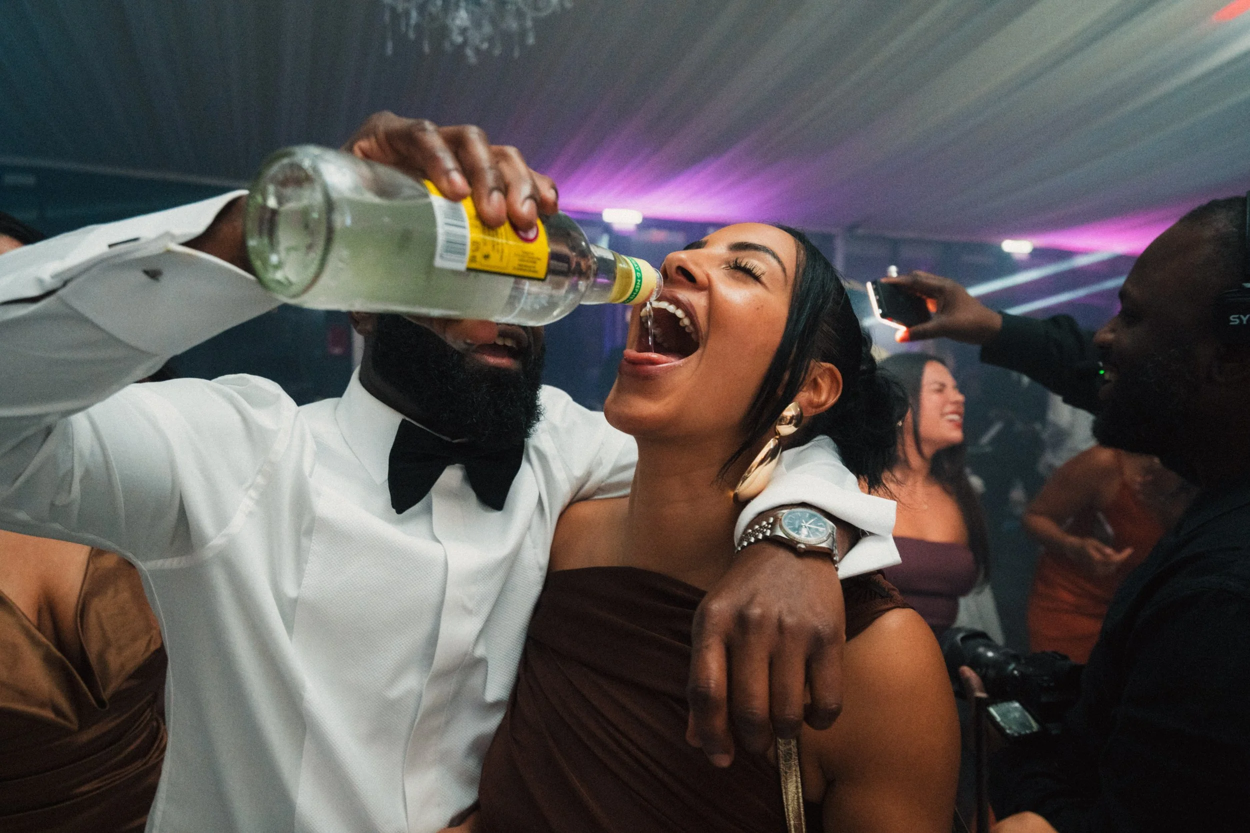 People dancing and drinking at a party with colorful lights and a lively atmosphere.