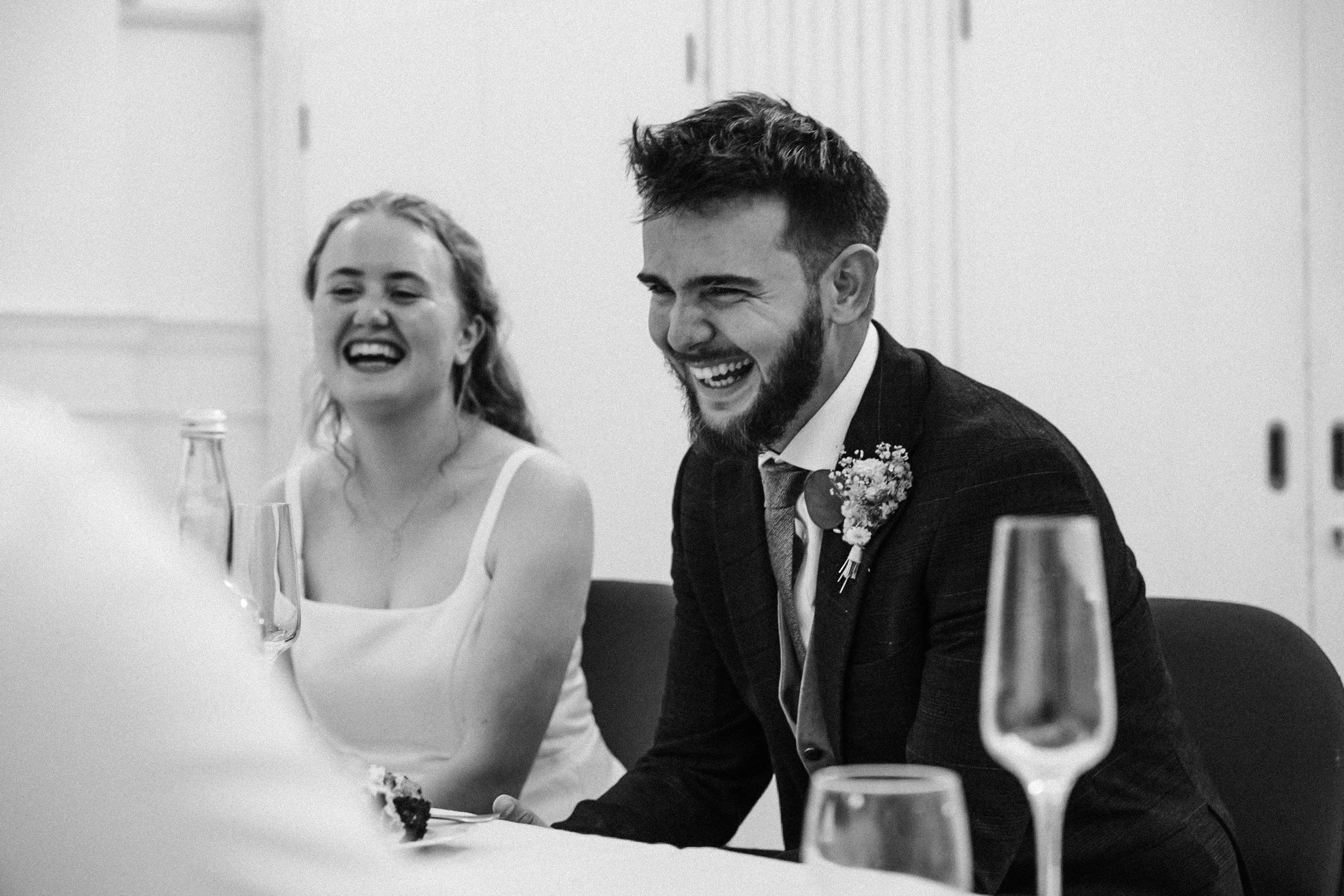 A man and woman laughing during a celebration, sitting at a table with glasses and bottles