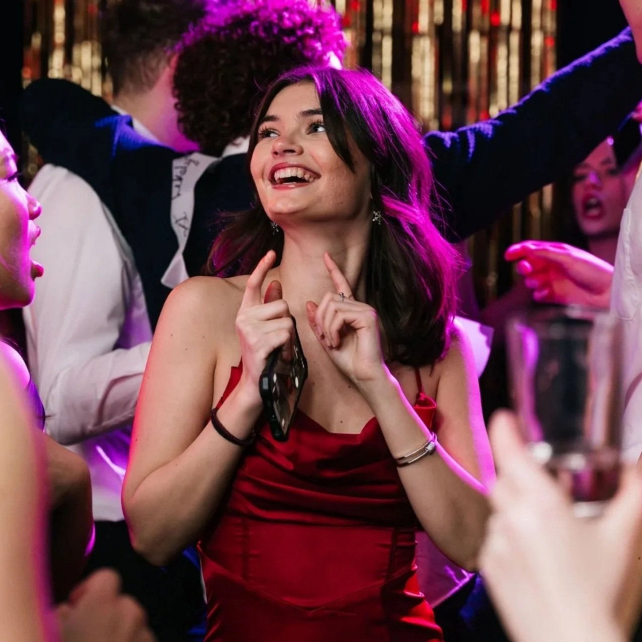 Young woman in a red dress smiling and dancing at a party with colorful lighting.