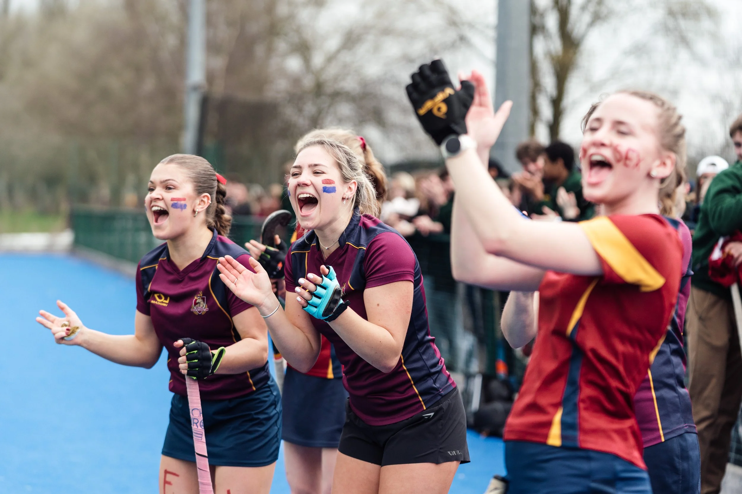 Female athletes celebrating after a sports event on a track field, with spectators in the background.