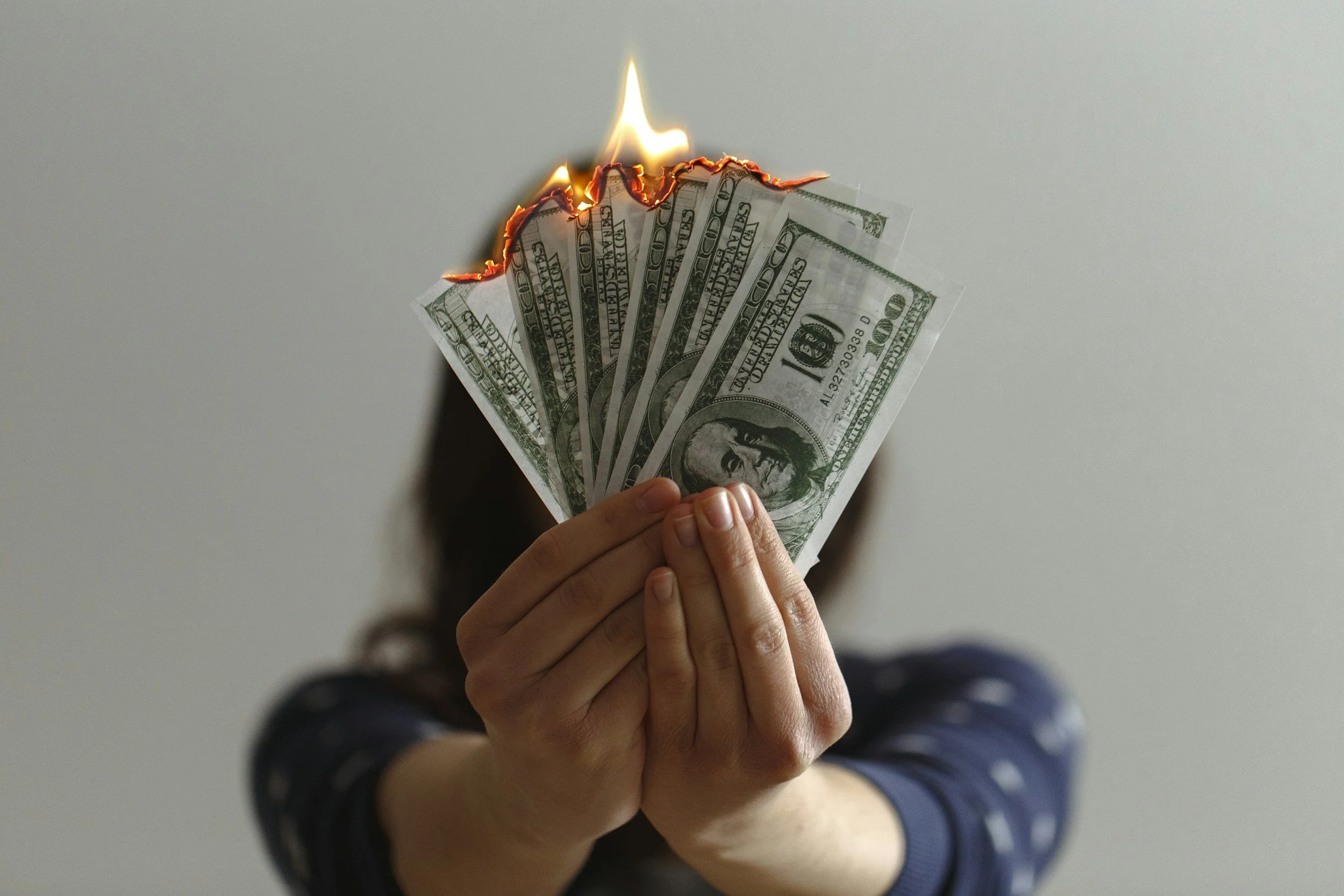 A depiction of a person holding dollar bills on fire.