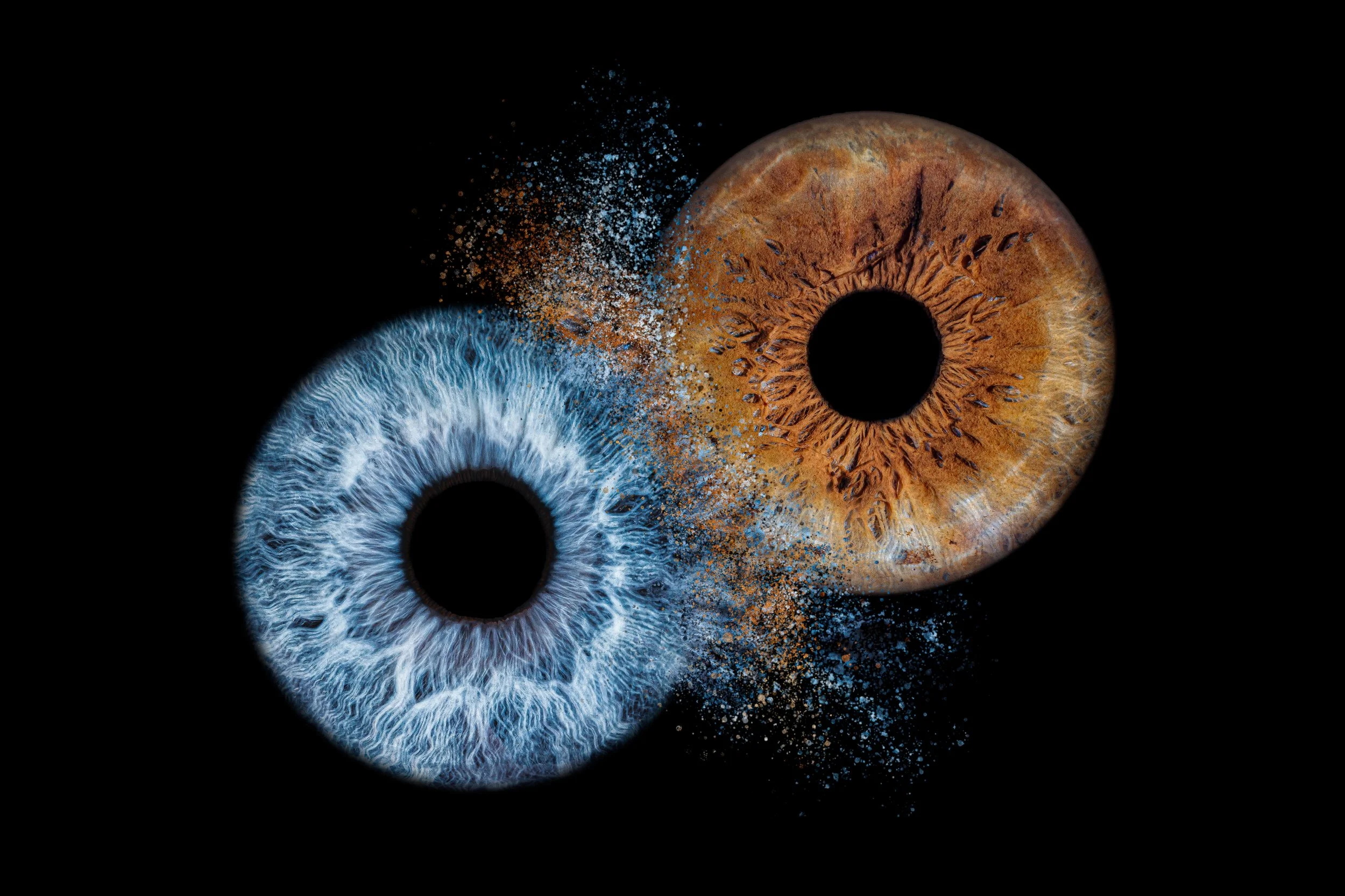Close-up of a blue eye and a brown eye against a black background, with colorful particles surrounding them.