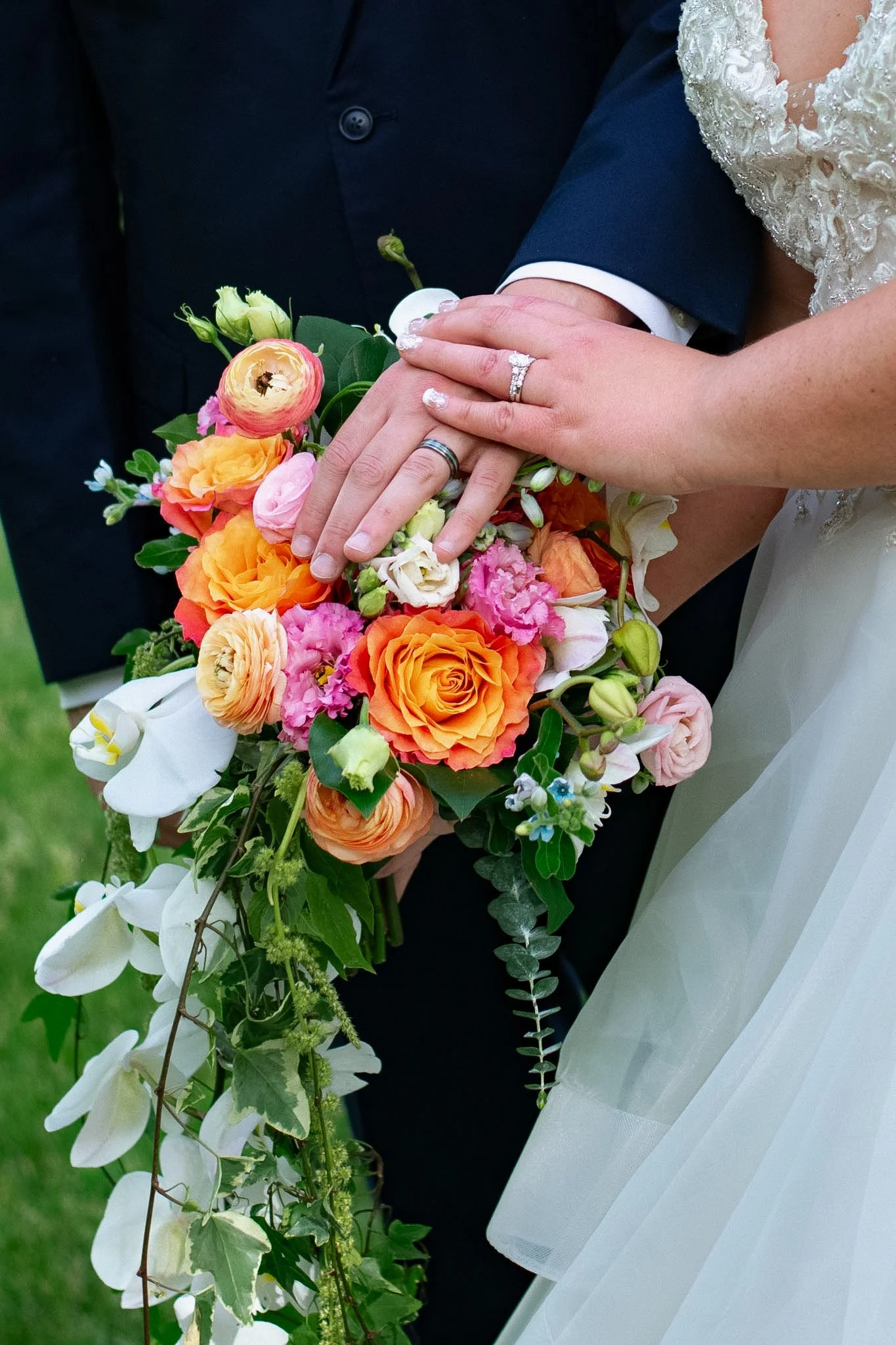 Close-up of a bride and groom's hands with wedding rings resting on a bouquet of colorful flowers, including roses and other blossoms.