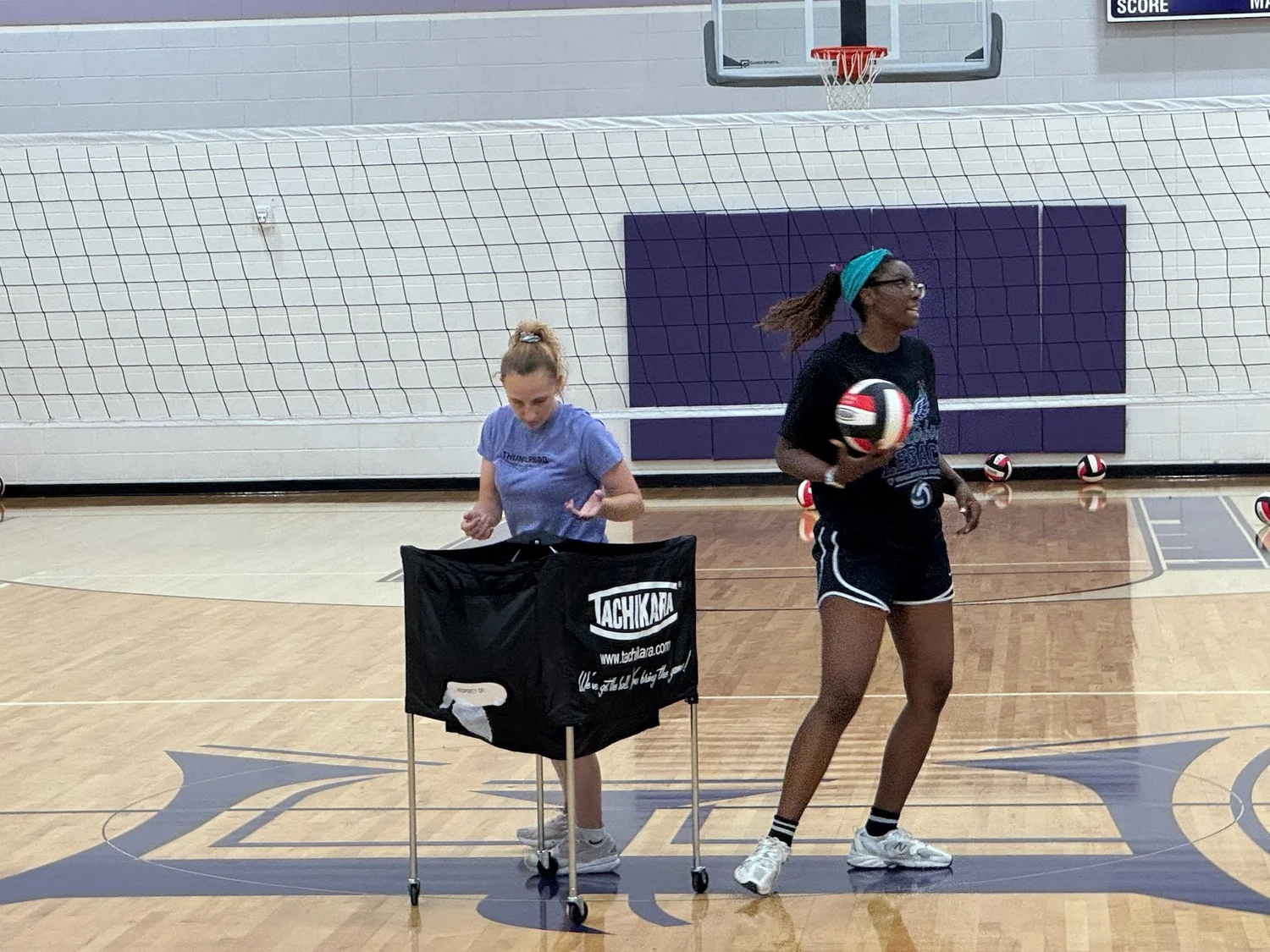 A coach and athlete beside a volleyball cart during camp.