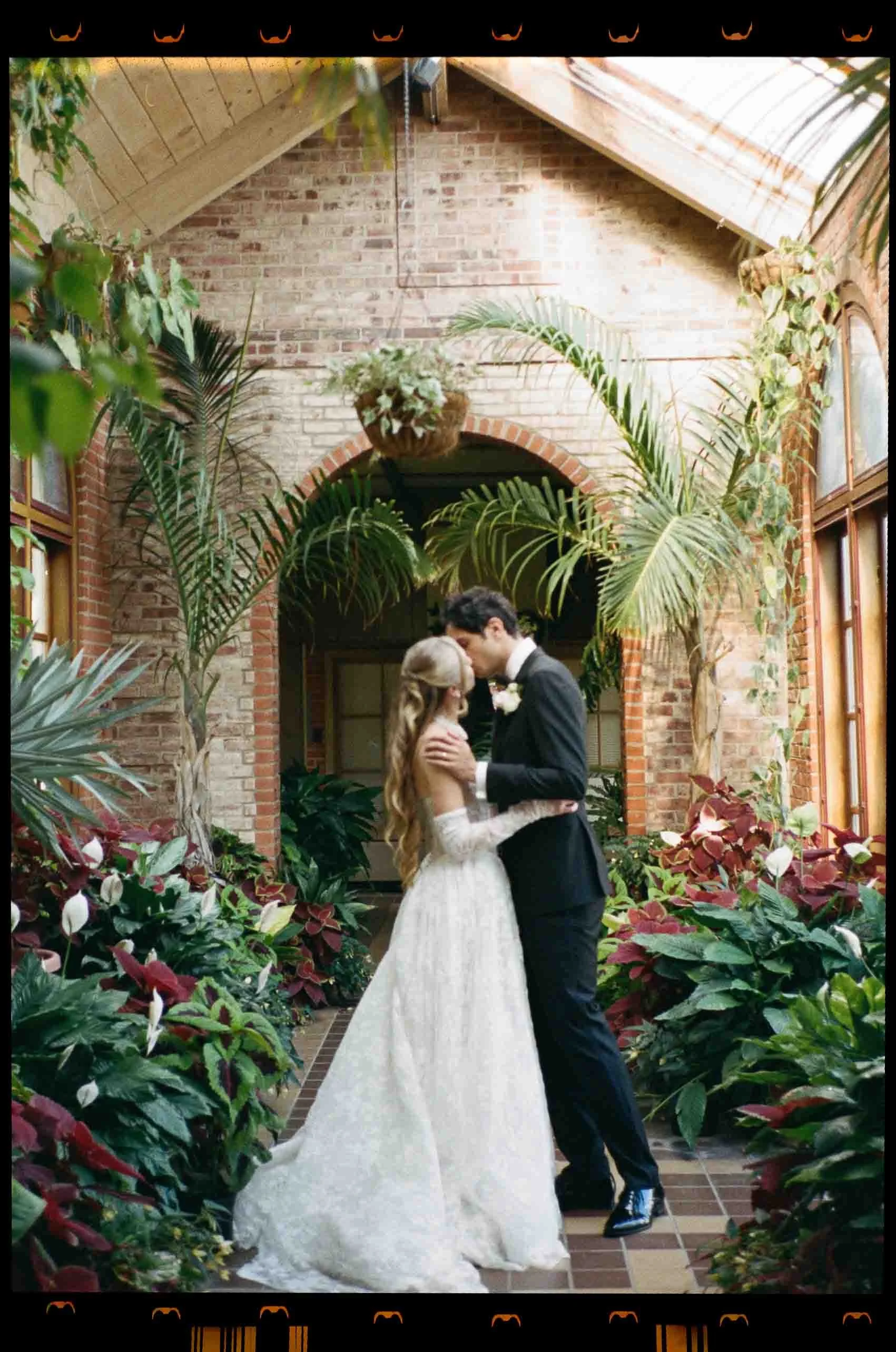 Film photography bride and groom kiss in a green house