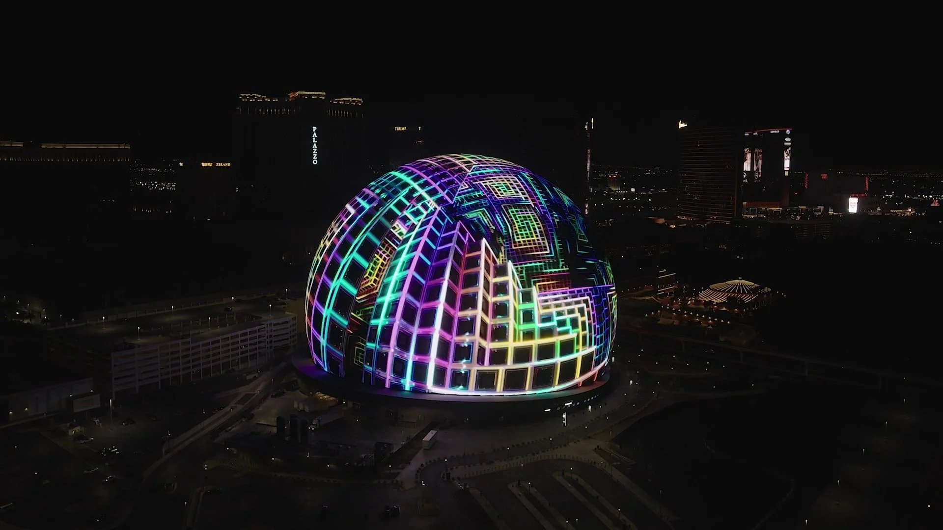 A spherical building illuminated with colorful neon lights forming geometric patterns at night.