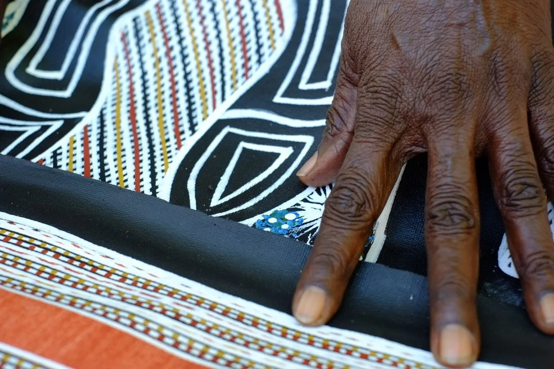 Close-up of an Elder's hand resting on her Aboriginal artwork.