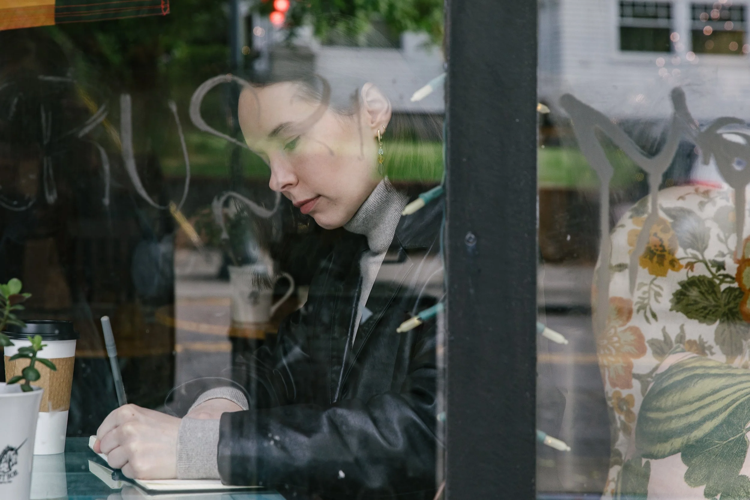 Photo of woman writing in a notebook taken through a window with graffiti