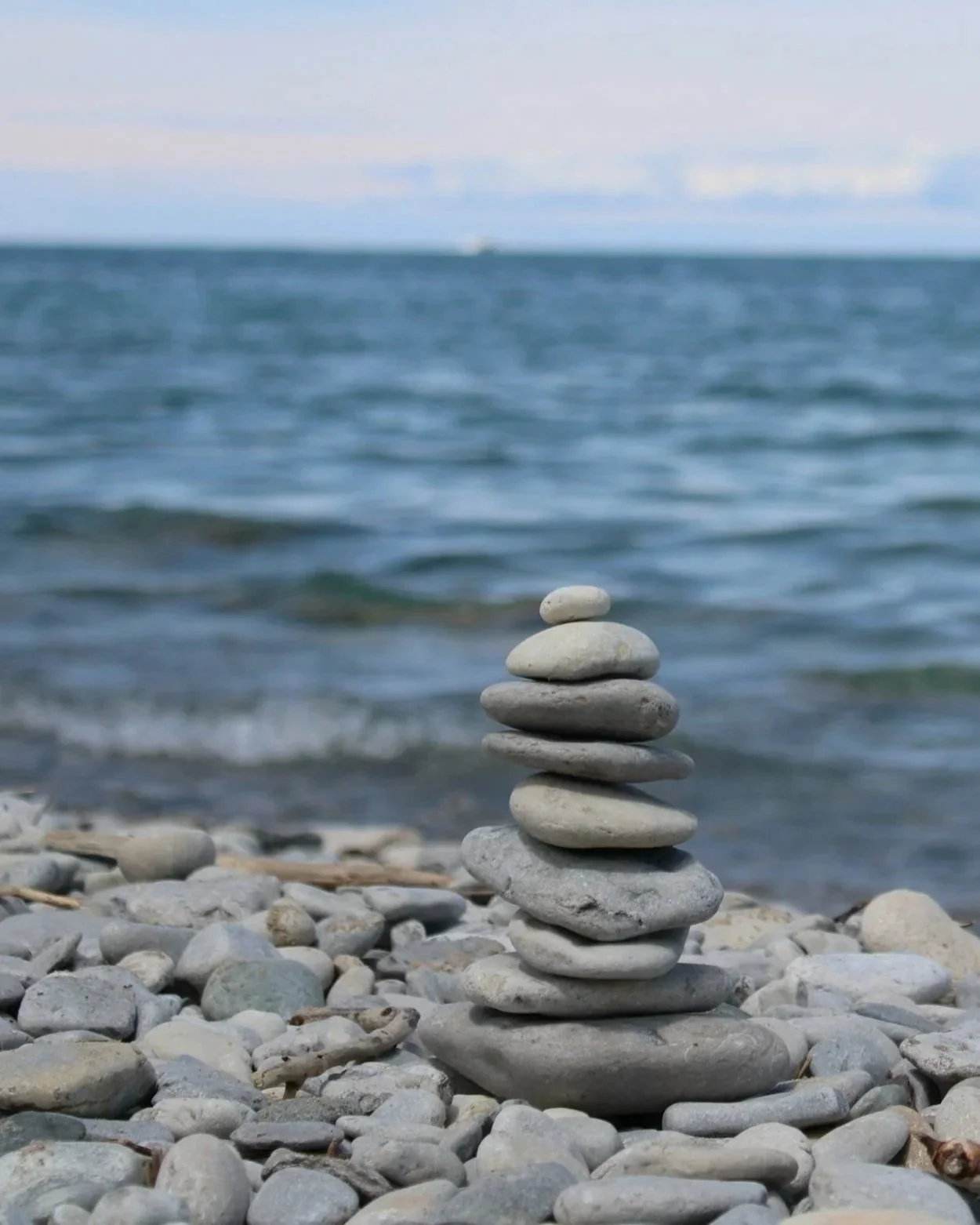 Stack of smooth gray stones on a pebble beach with a blurred ocean in the background.