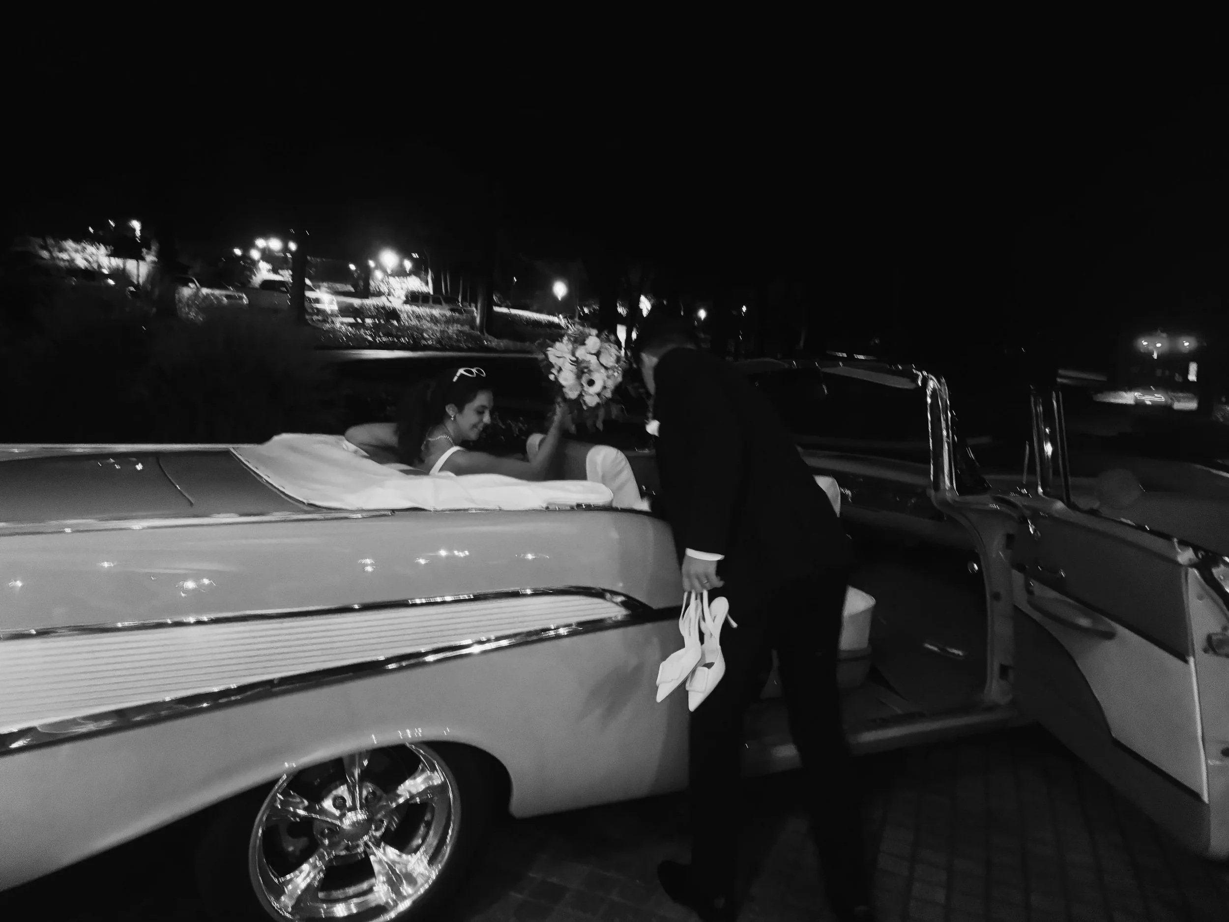 Bride and groom making a nighttime send-off in a vintage car, a classic wedding exit moment.