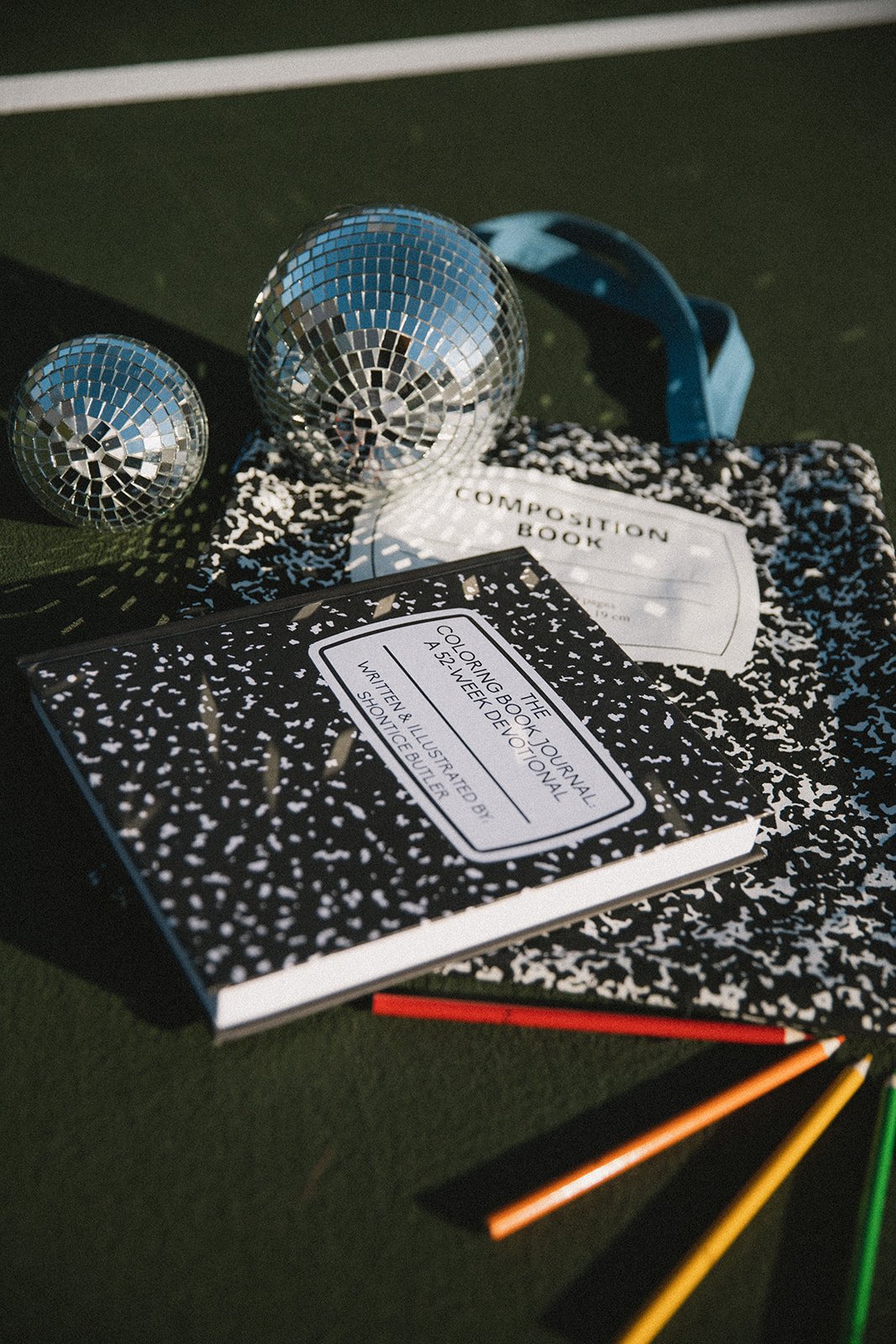 A composition notebook, a journal titled "The Composing Journal," disco balls, colored pencils, and a white card with black text on a textured background.