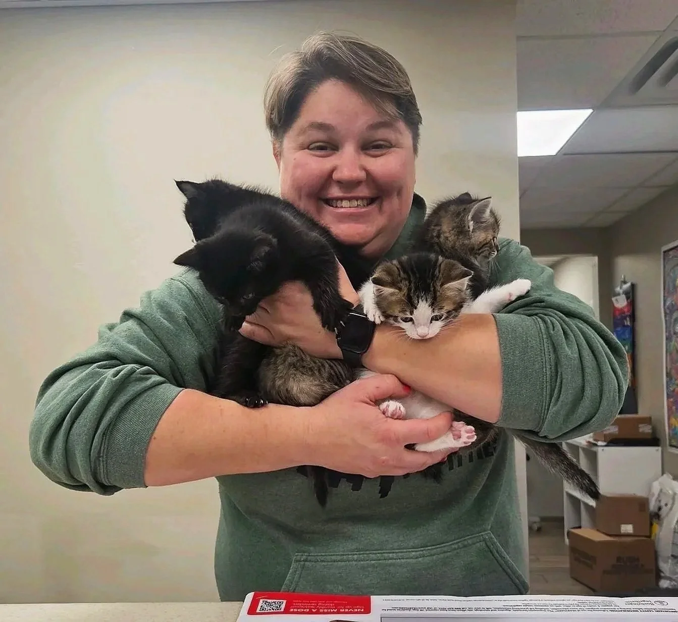 A person smiling and holding four cats of different colors and patterns.