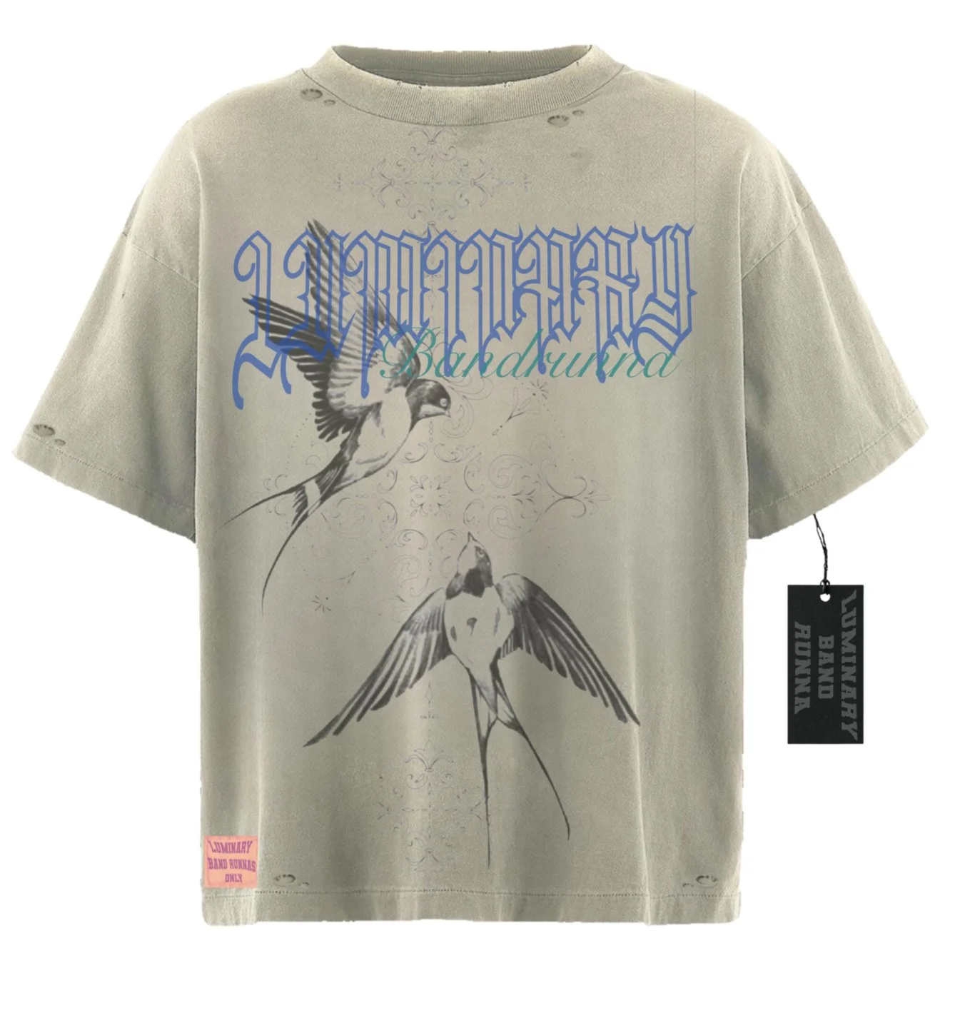 Beige T-shirt with graphic design of two birds, one flying and one perched. The shirt has blue and green text reading 'LUMINARY BACKDUNA' and a pink label at the bottom left corner that says 'LUMINARY BAND RAKKA'S ONLY.' There is a black hanging tag 