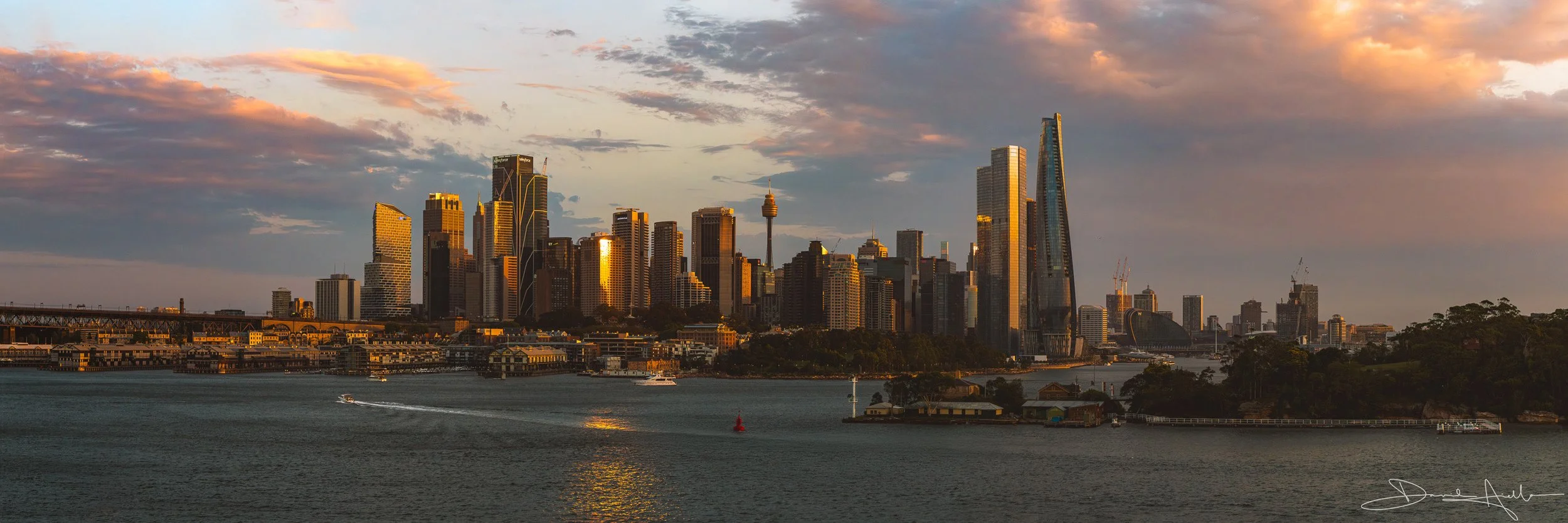 Sydney skyline at sunset with high-rise buildings and a harbor in the foreground.