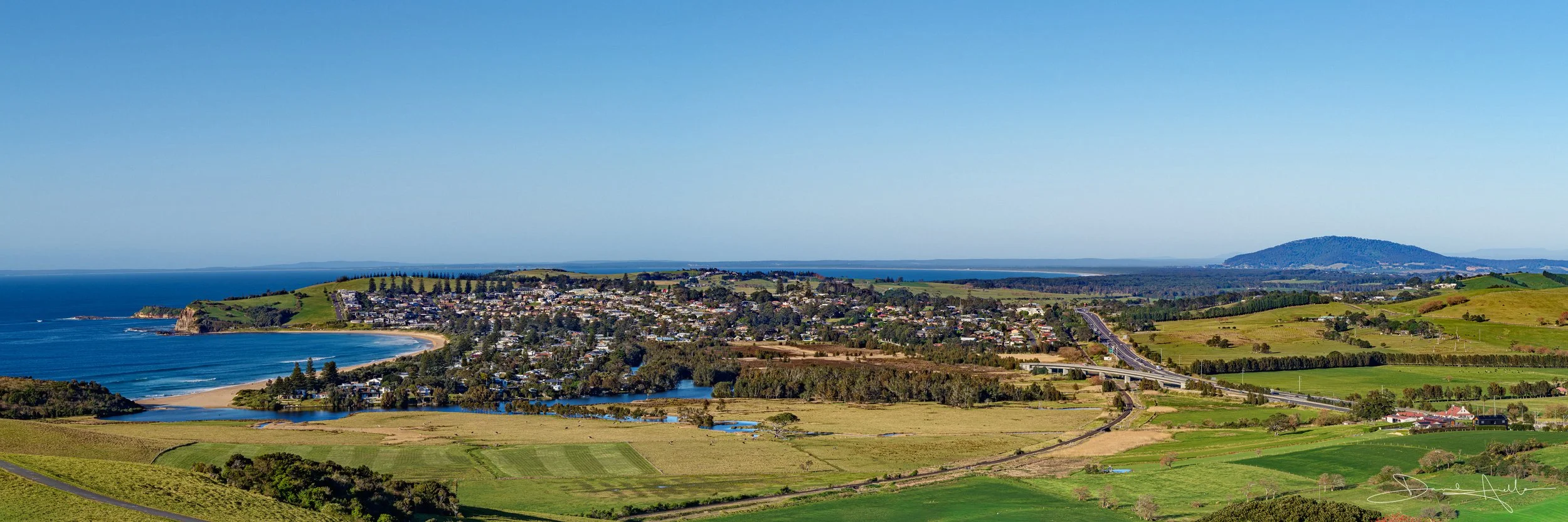 A scenic view at a high altitude over-looking lush green hills and deep blues of the ocean. 