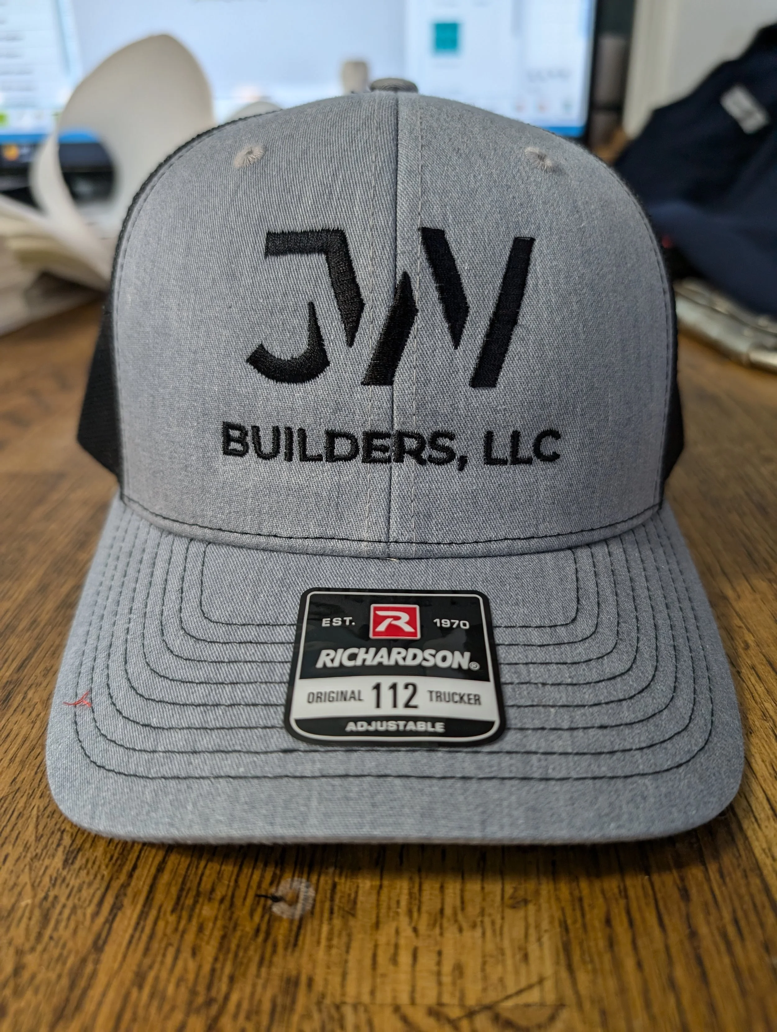 Gray Richardson trucker cap with black logo and text, placed on a wooden table.