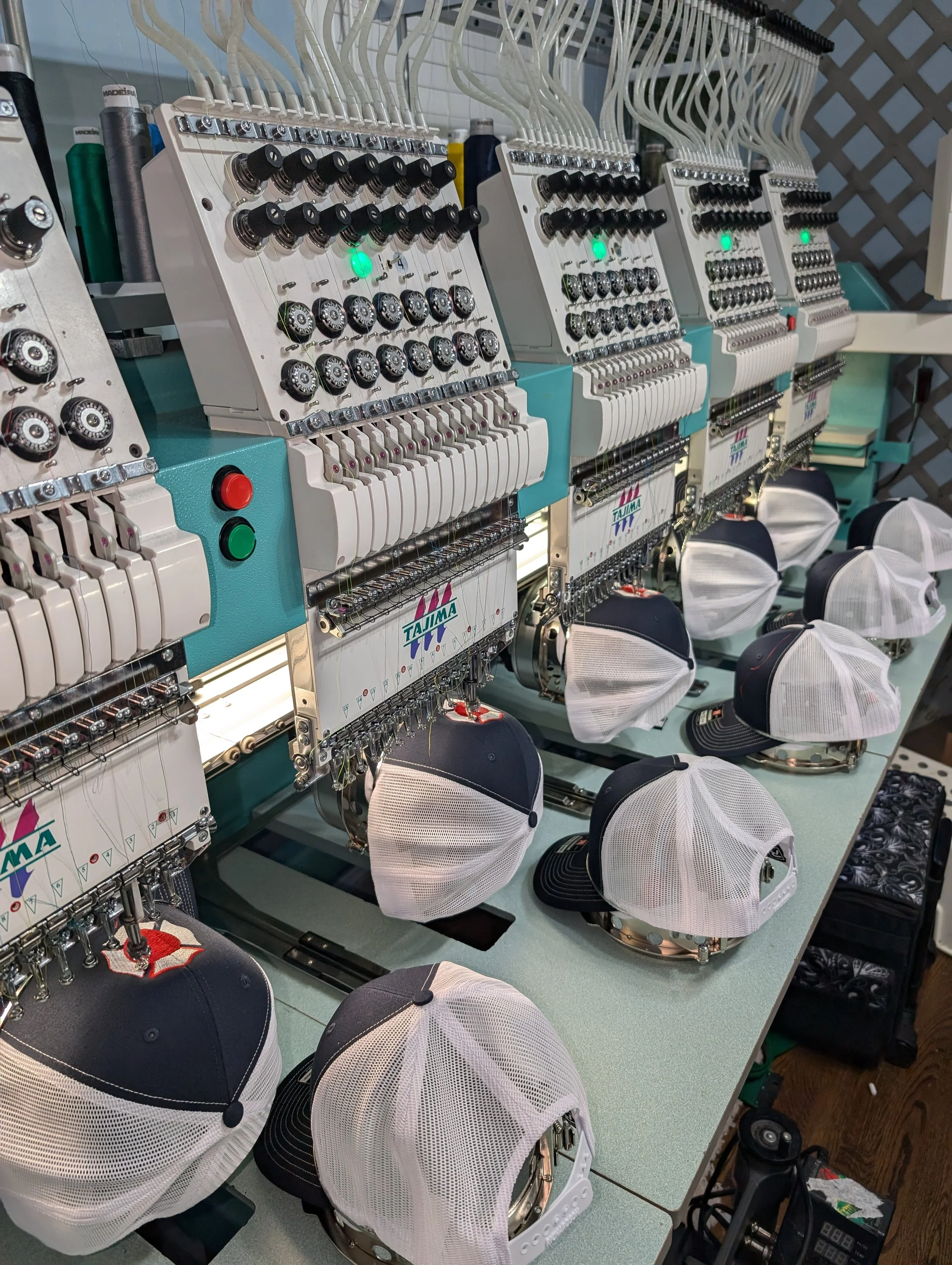 Multiple embroidery machines stitching designs on baseball caps, with hats placed underneath.