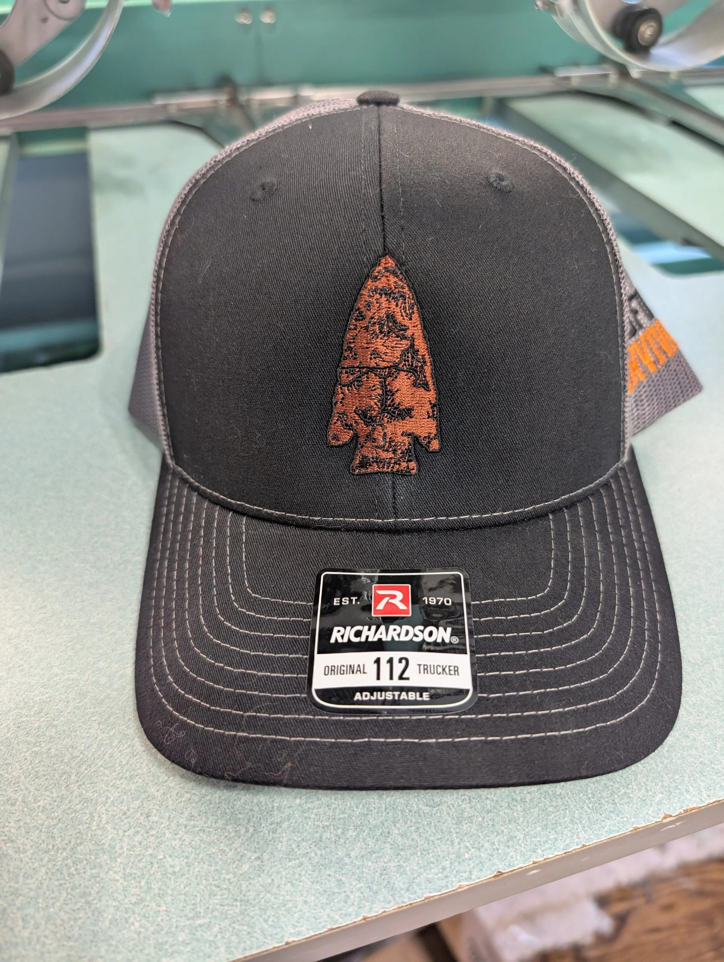 Black Richardson trucker hat with a stylized orange tree logo on the front and the word 'AUTOMOTIVE' on the side, placed on a light-colored surface.