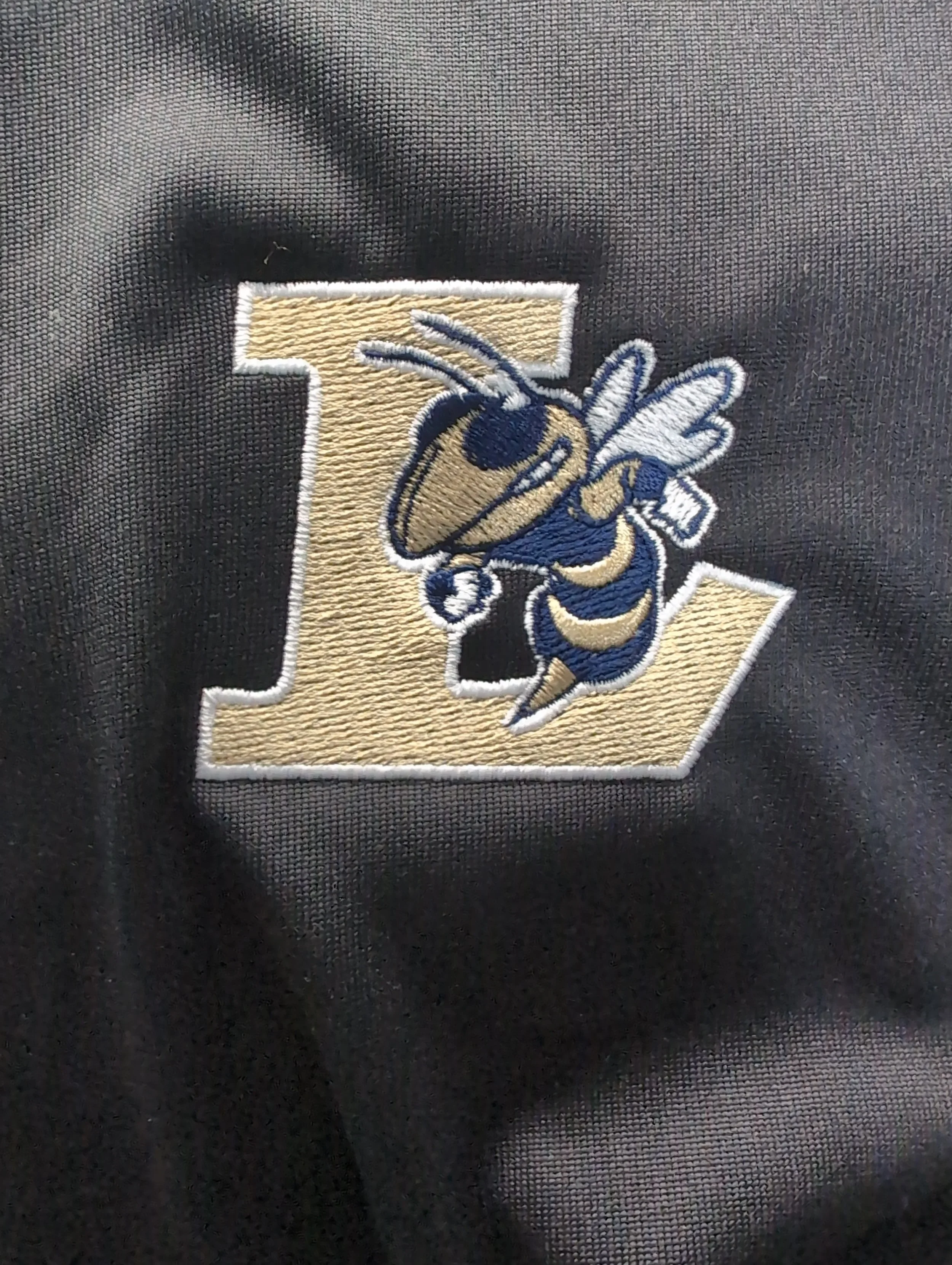 Embroidered logo of a bee with sunglasses and wings, placed on a letter 'L' on black fabric.