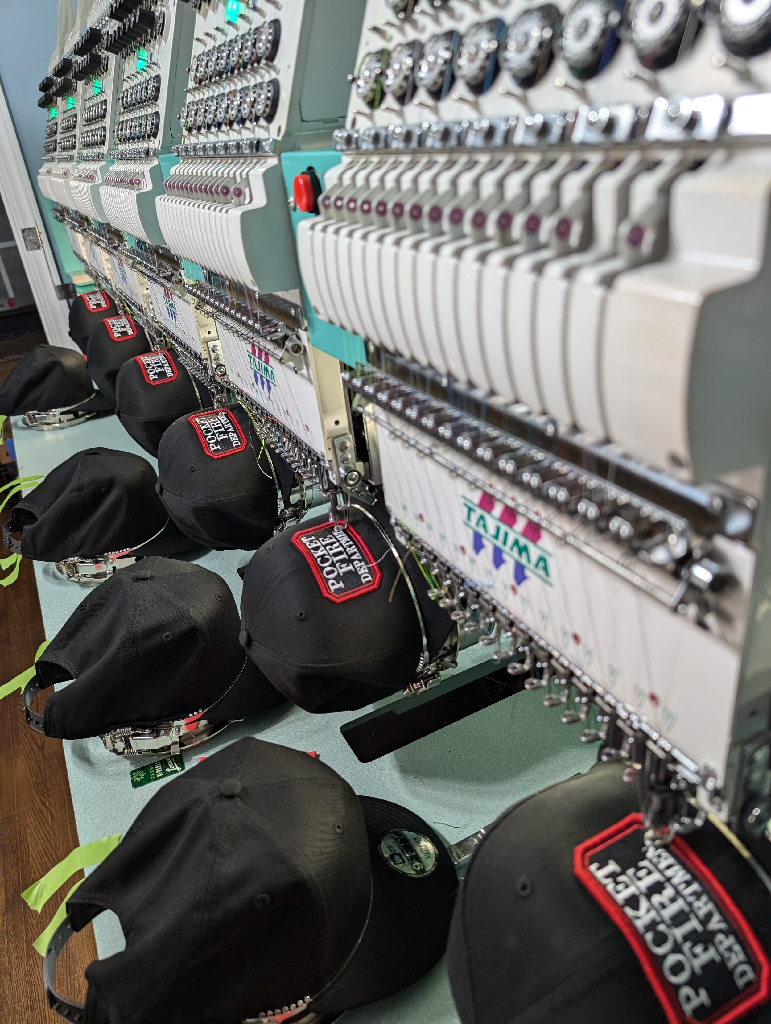 Black caps with red and white patches on a sewing machine embroidery station.