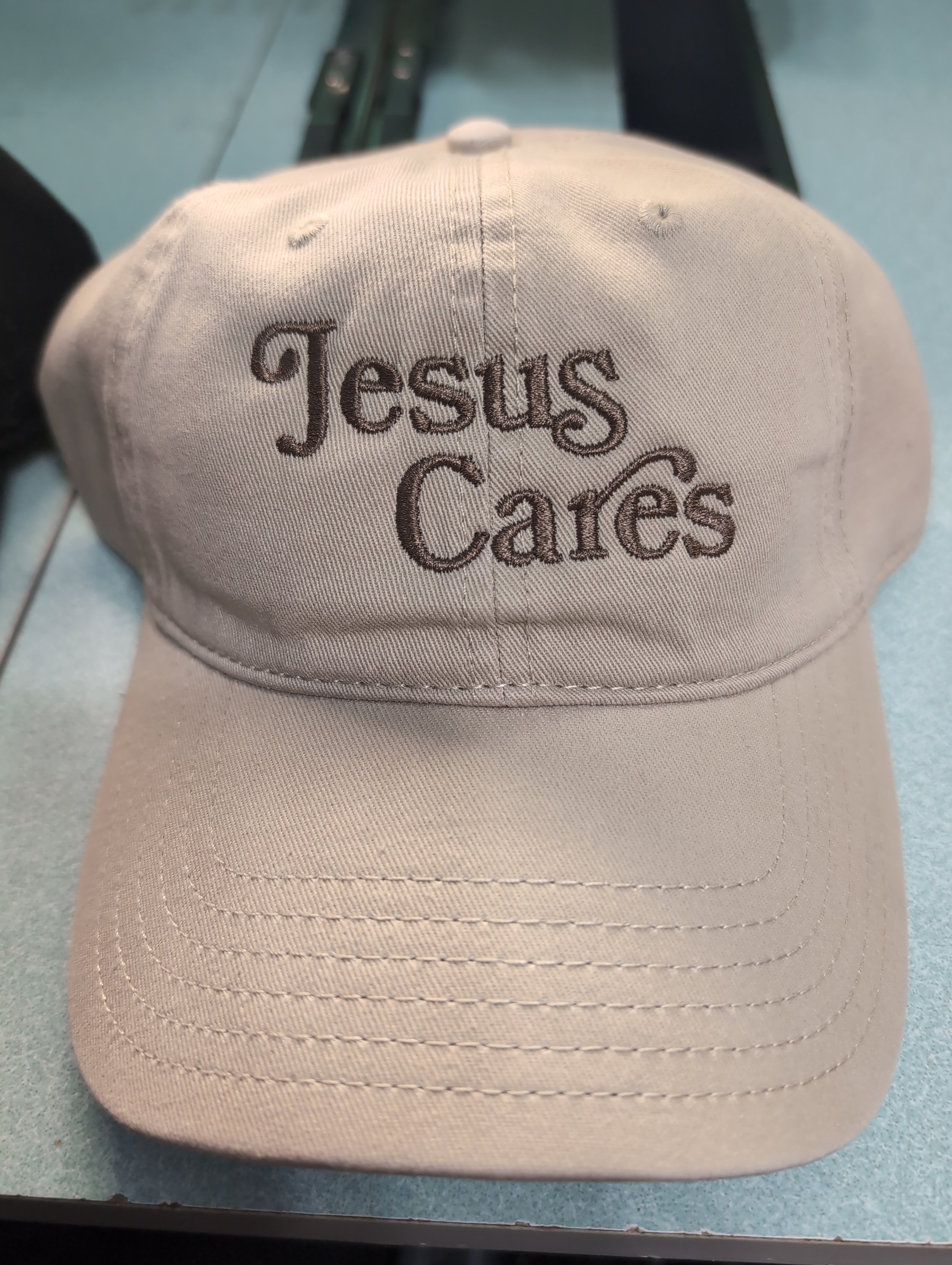 Beige baseball cap with embroidered text 'Jesus Cares' on the front.