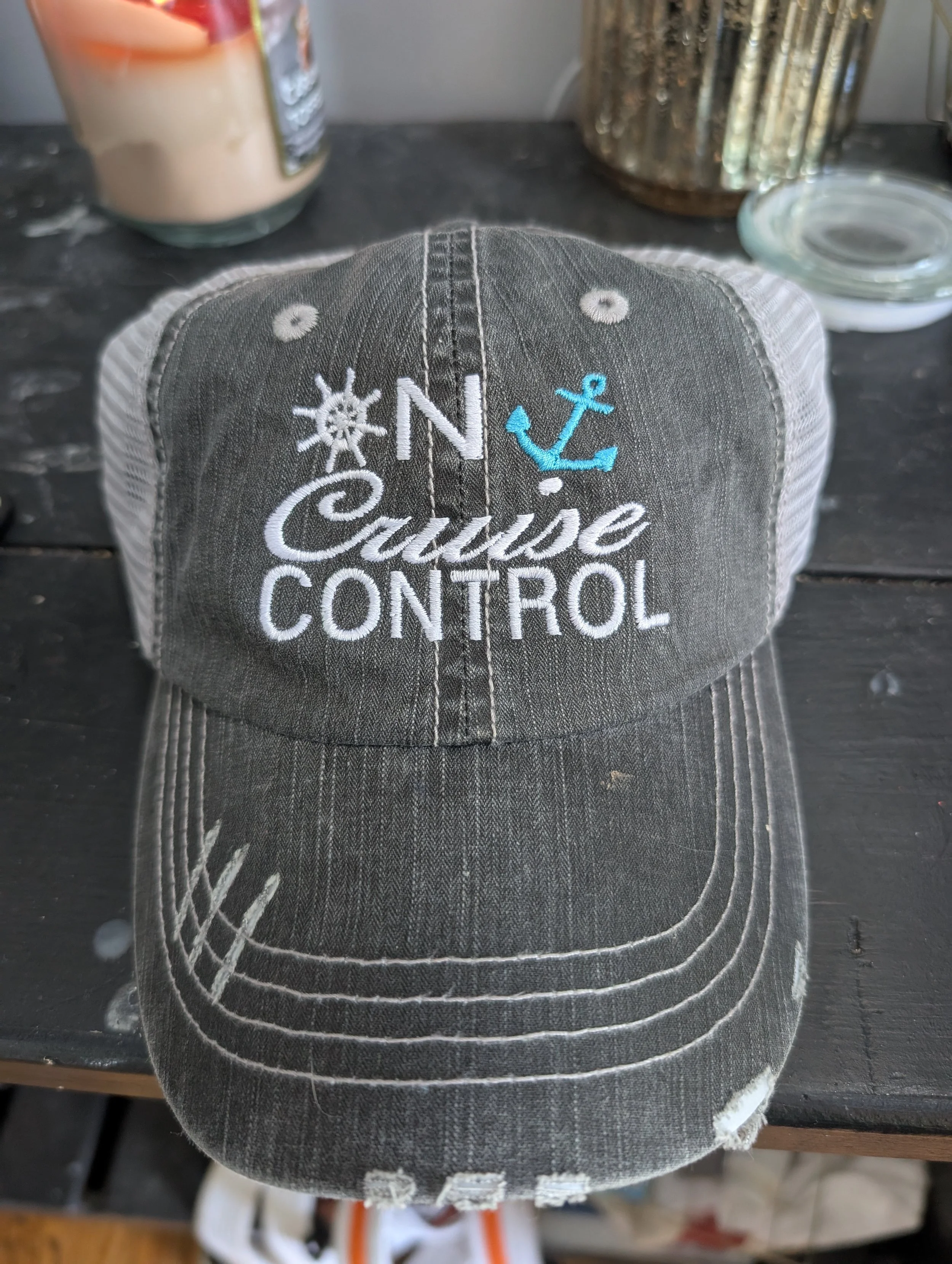A dark gray trucker cap with white mesh back. It has embroidered text and symbols: a ship's wheel, an anchor, and the words 'N' and 'Cuisse CONTROL'.