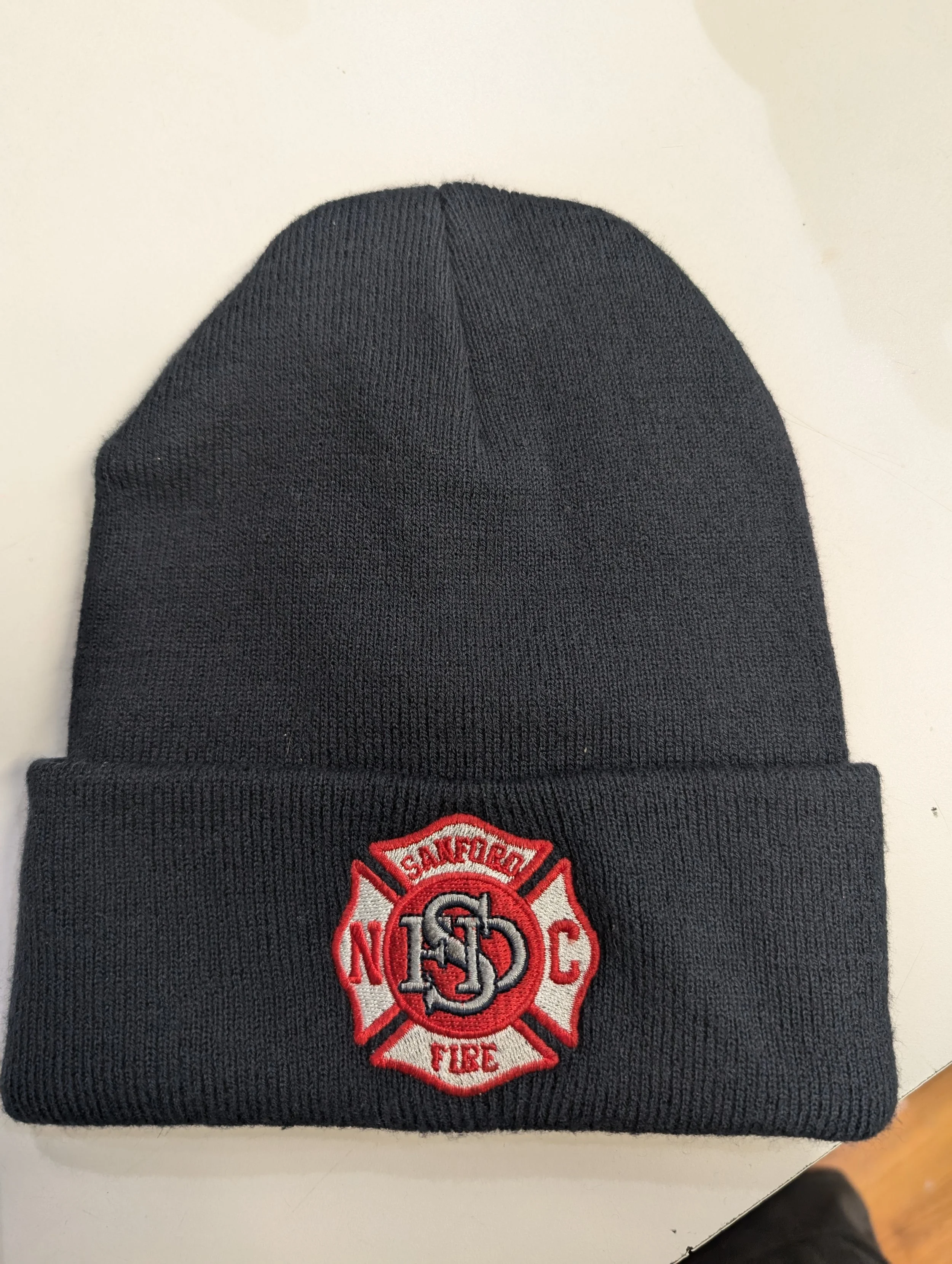 Black firefighter knit beanie with a red, white, and black sewn patch of a fire department emblem reading 'Saulkport Fire'.