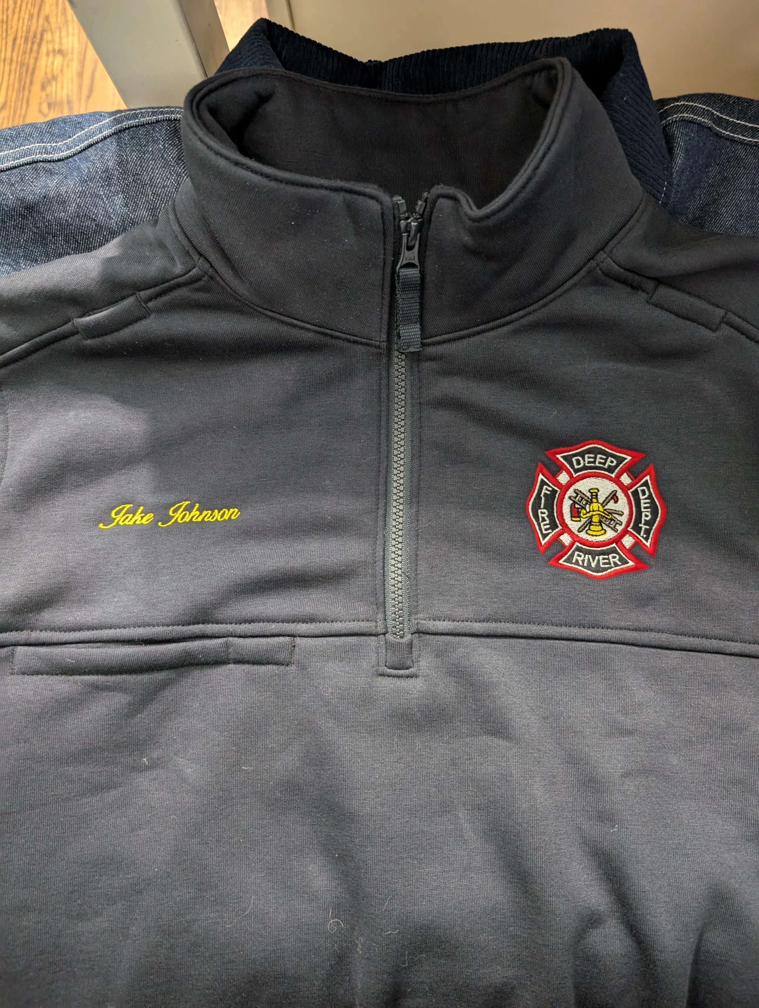 A black uniform with a firefighter badge and yellow embroidered name 'Jake Johnson' on the chest.
