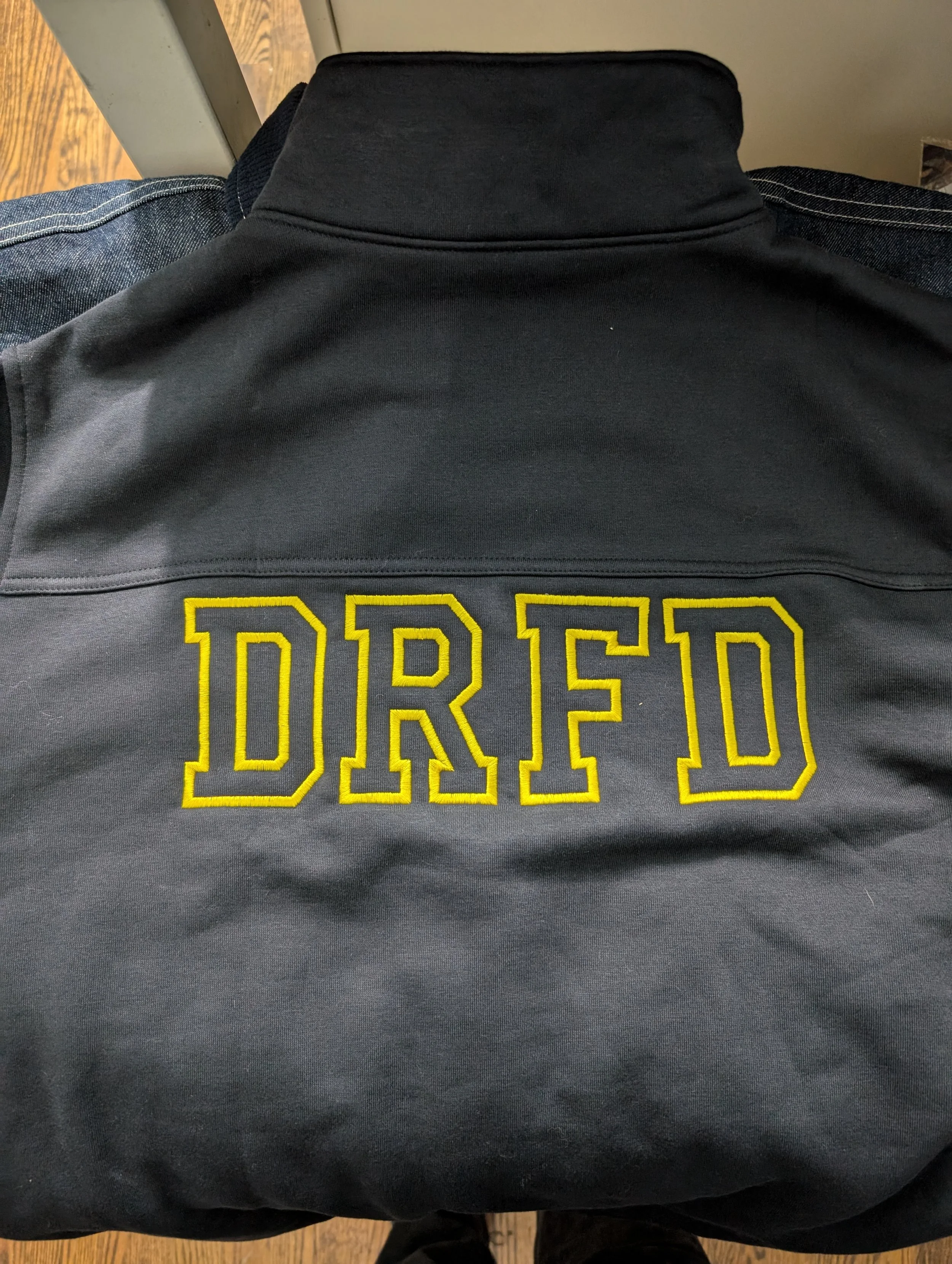 Back of a gray jacket with yellow embroidered letters spelling 'DRED' on the back.