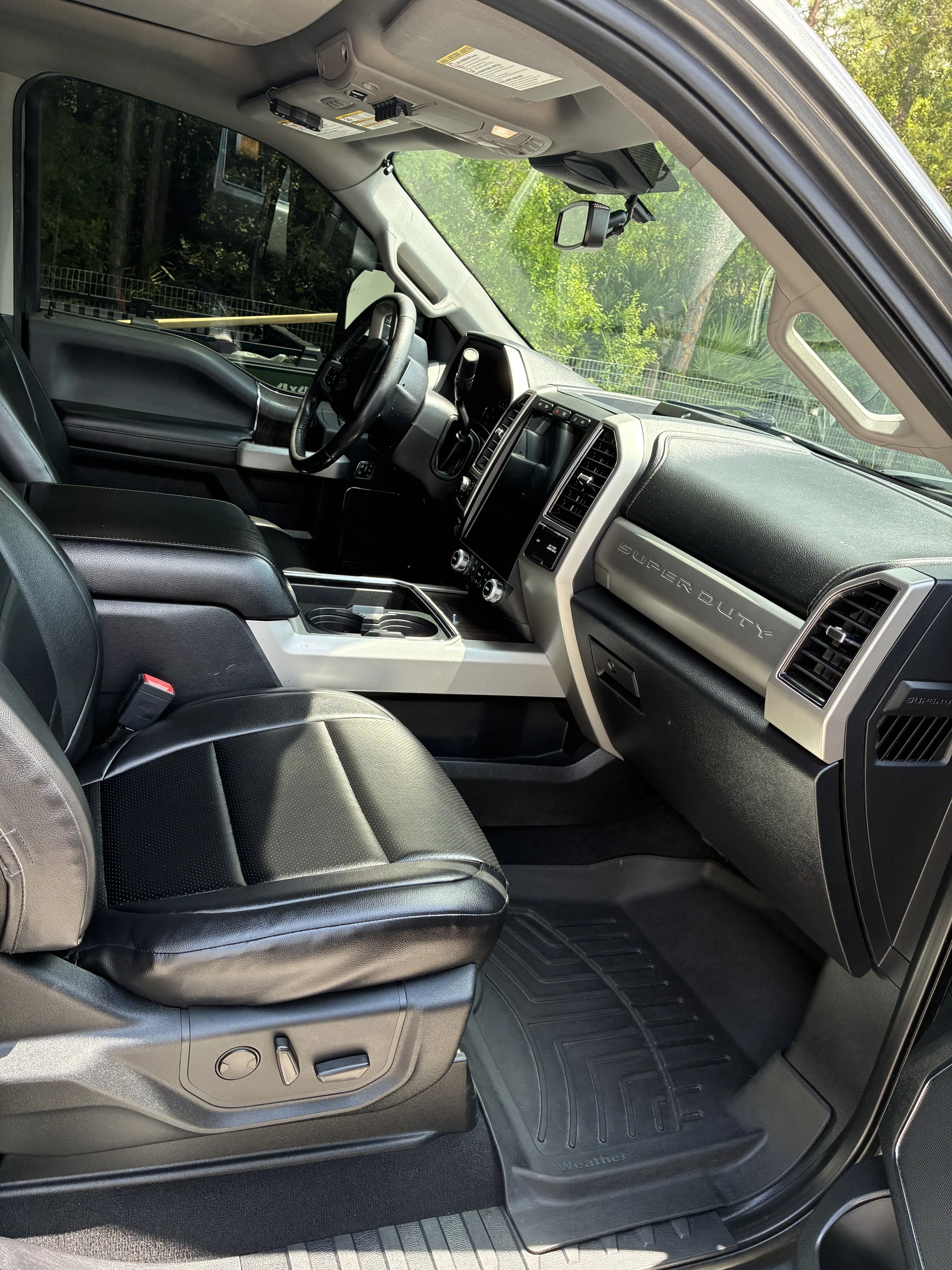 Interior of a black pickup truck with leather seats, a large touchscreen display on the dashboard, and a console with cup holders.