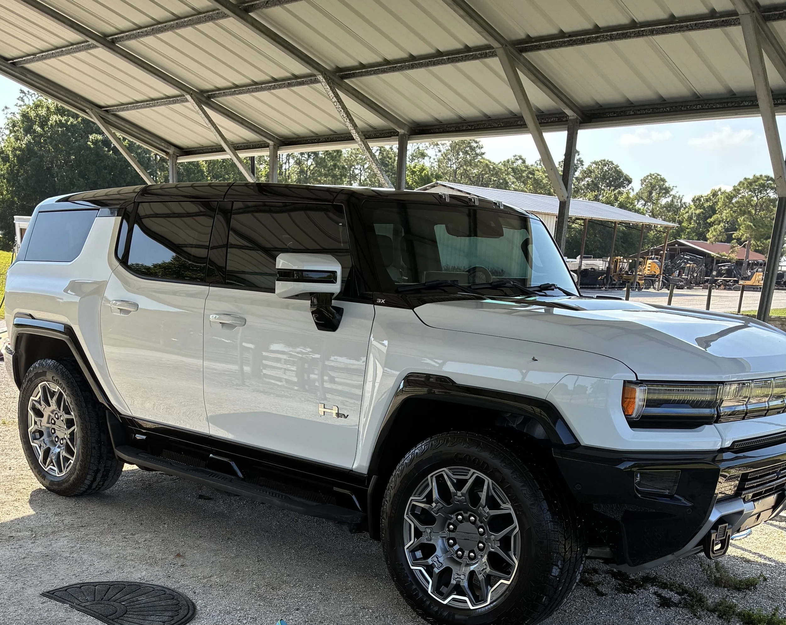 A white electric pickup truck with black accents parked under a metal carport on a sunny day.