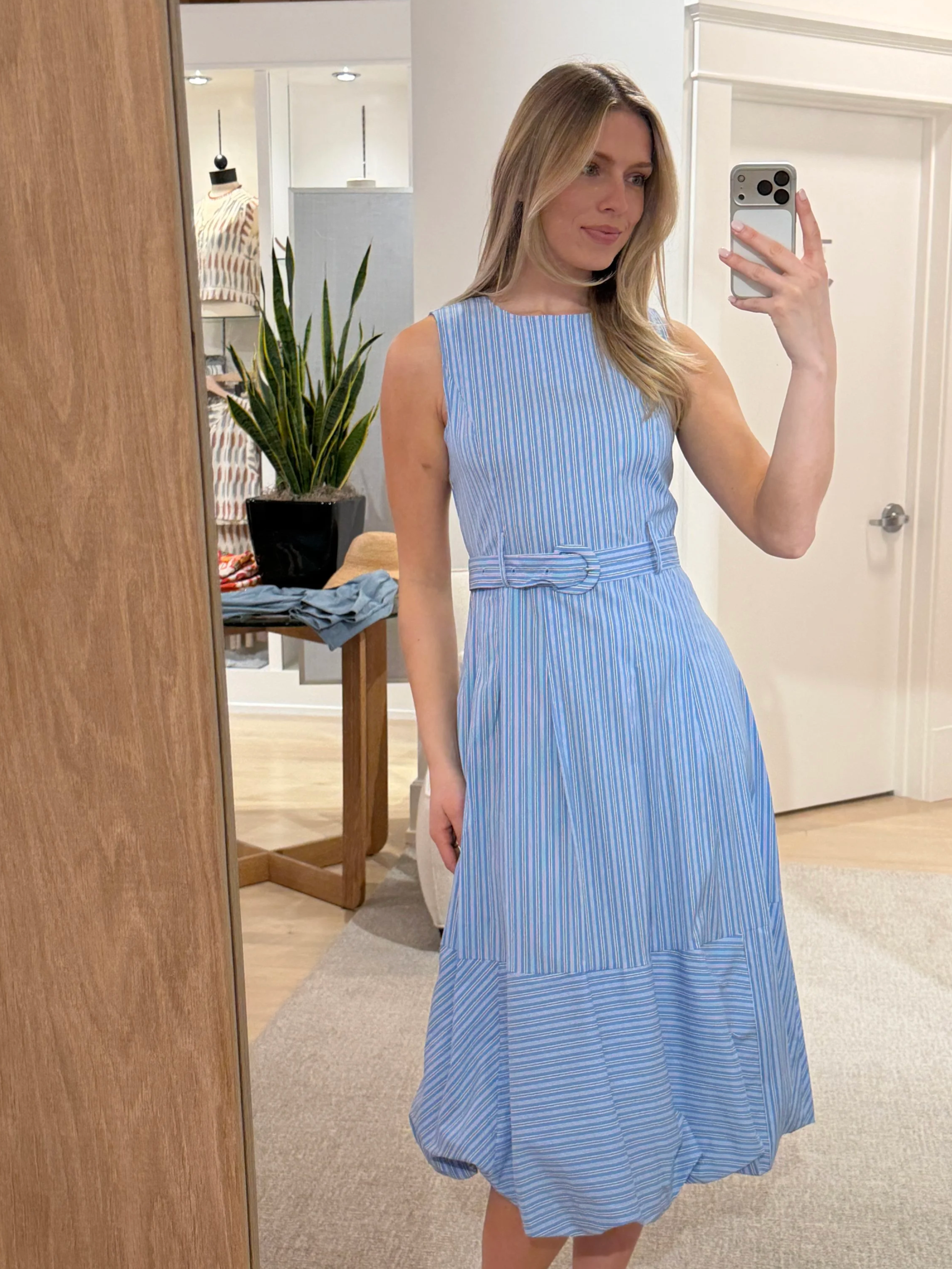 A woman taking a mirror selfie in a fitting room, wearing a blue and white striped dress.
