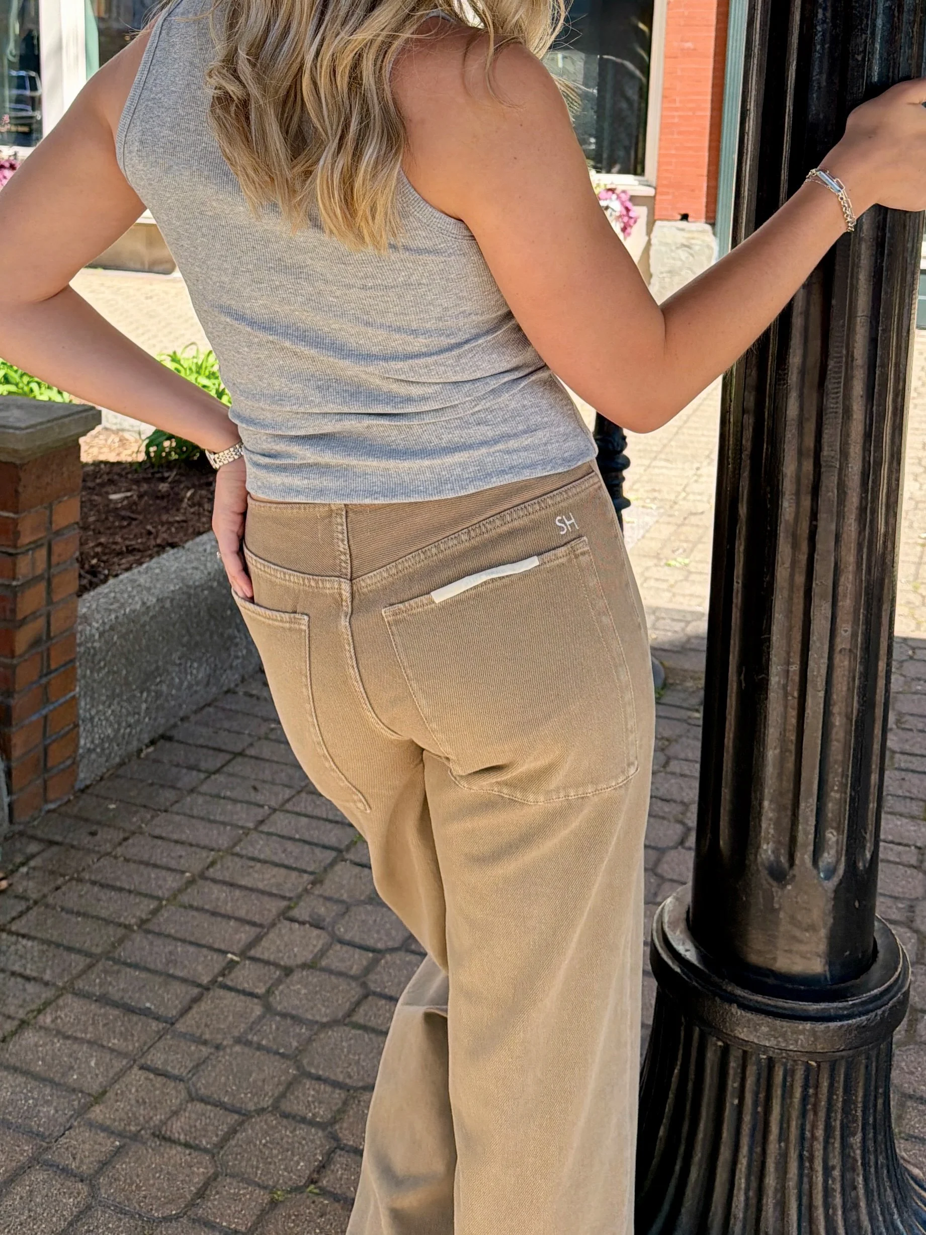 A woman wearing a gray sleeveless top and beige pants standing outside near a black metal lamppost.