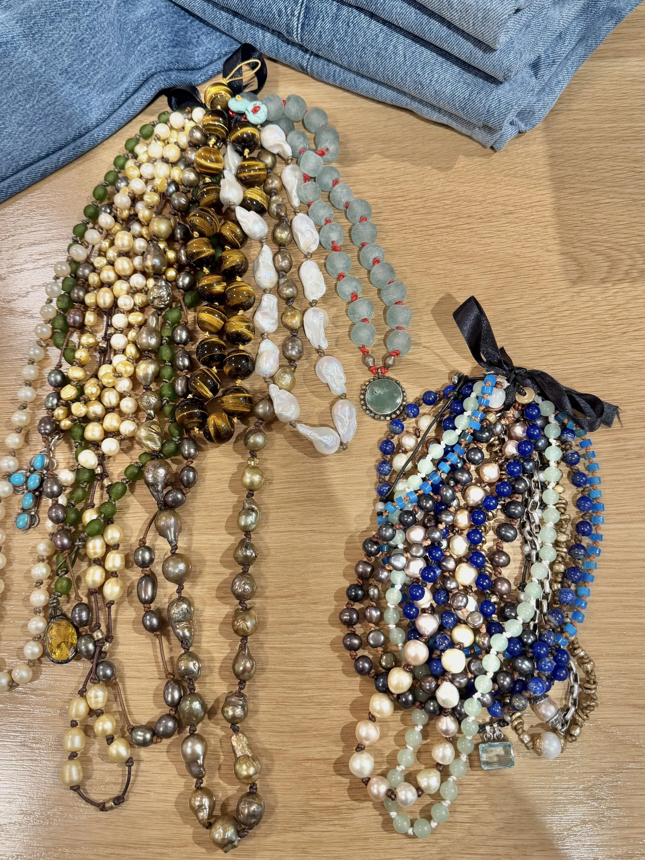 Multiple strands of various types of pearl necklaces on a wooden surface with blue fabric in the background.