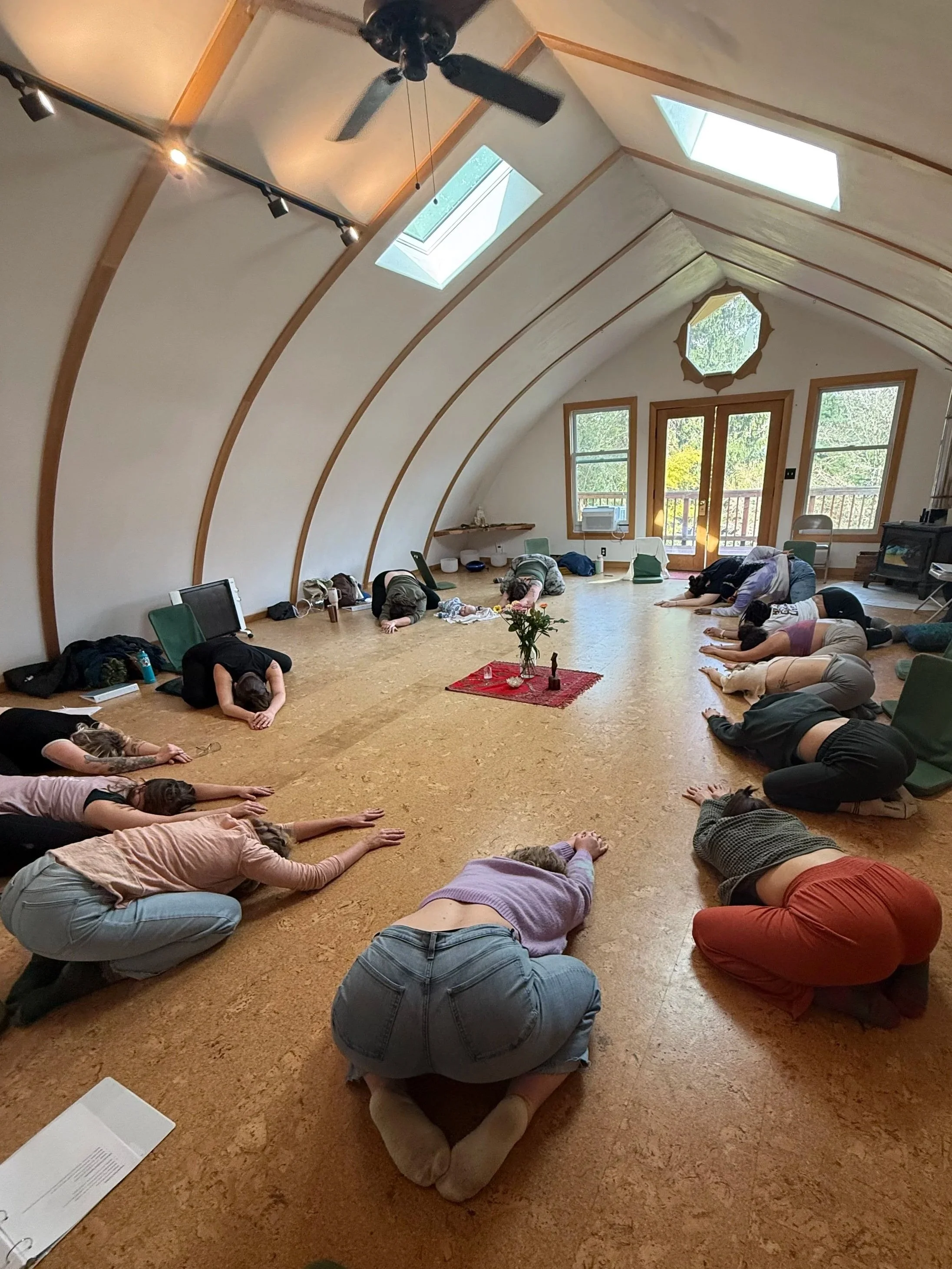 People practicing yoga in a spacious, bright room with a high, curved ceiling, skylights, and large windows.
