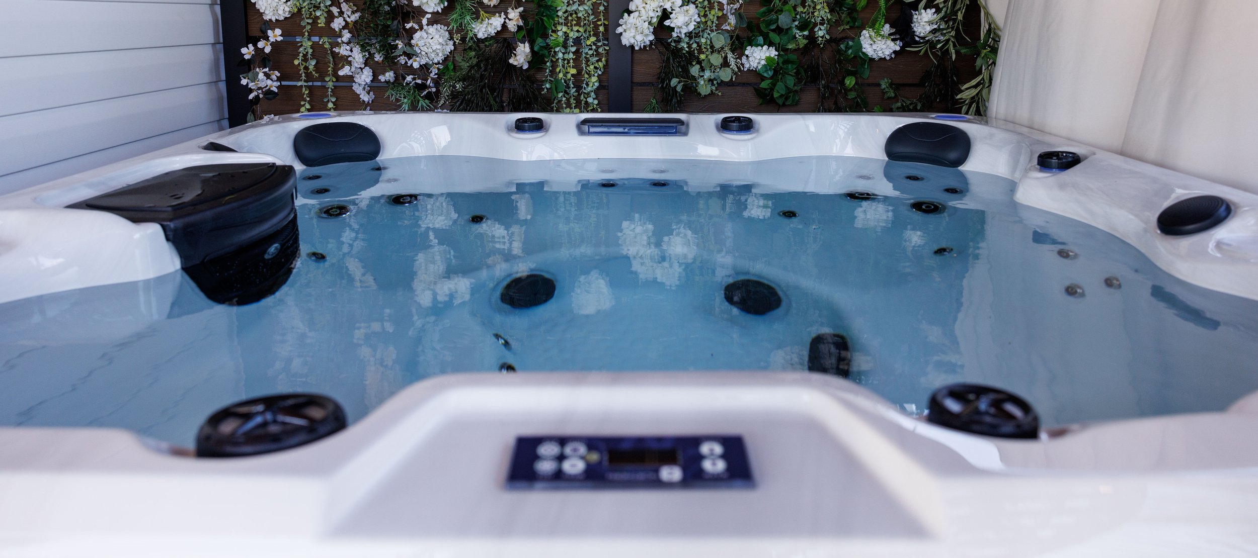 A hot tub filled with clear balanced water, topside control panel in view