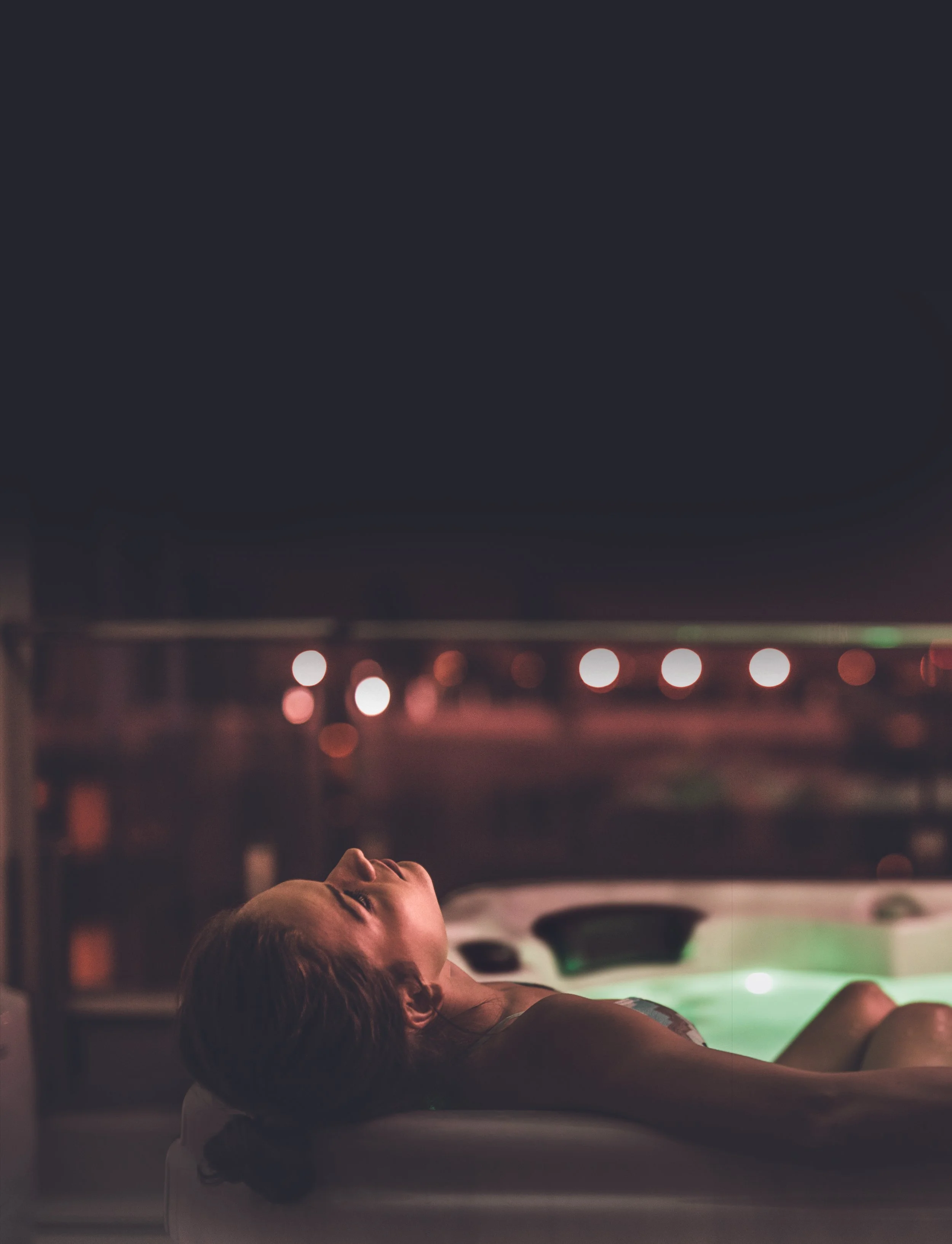 A woman lying on a tanning bed in a dimly lit room with blurred colorful lights in the background.