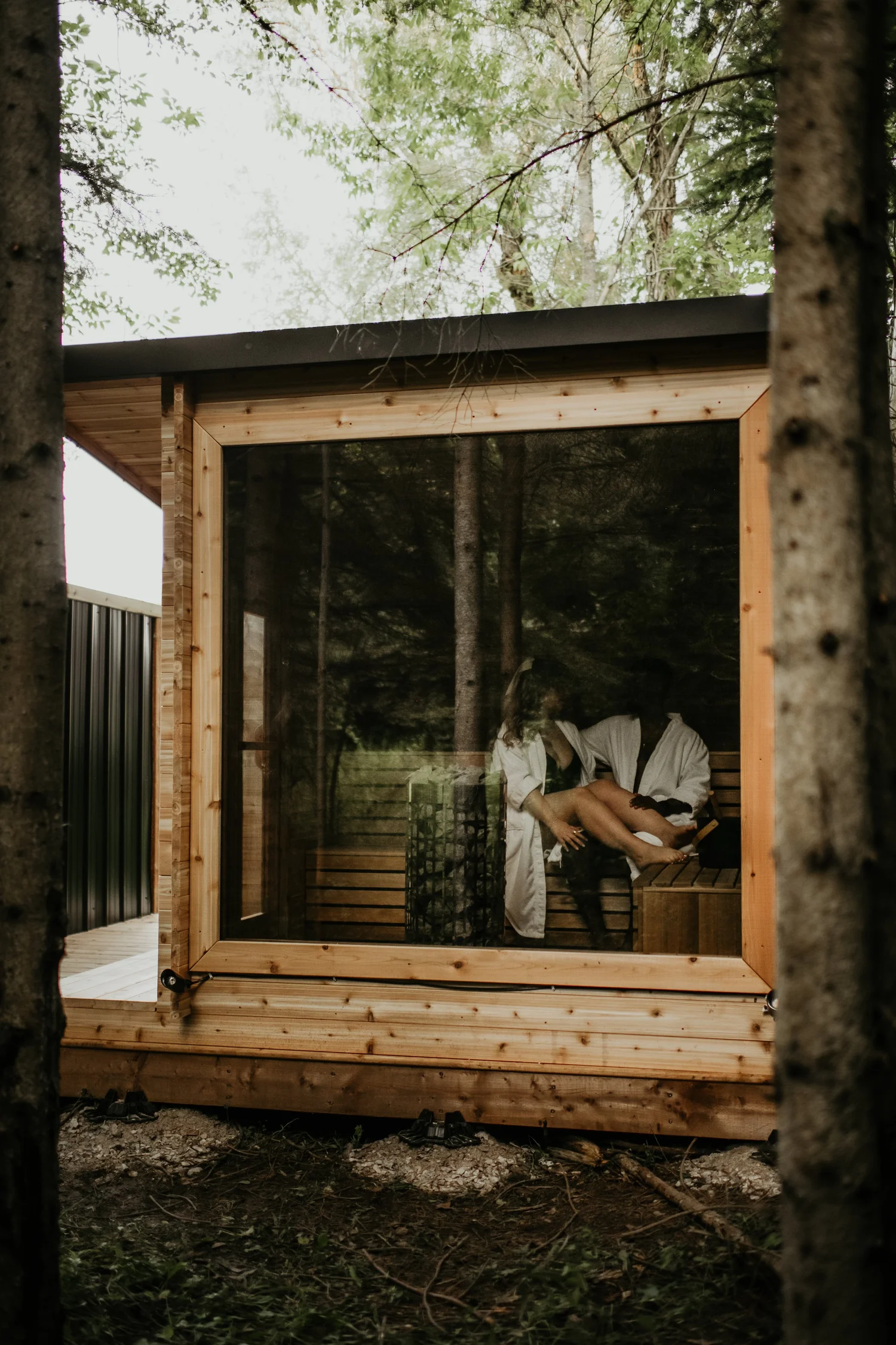 Two people relaxing inside a glass fronted cedar sauna in the woods