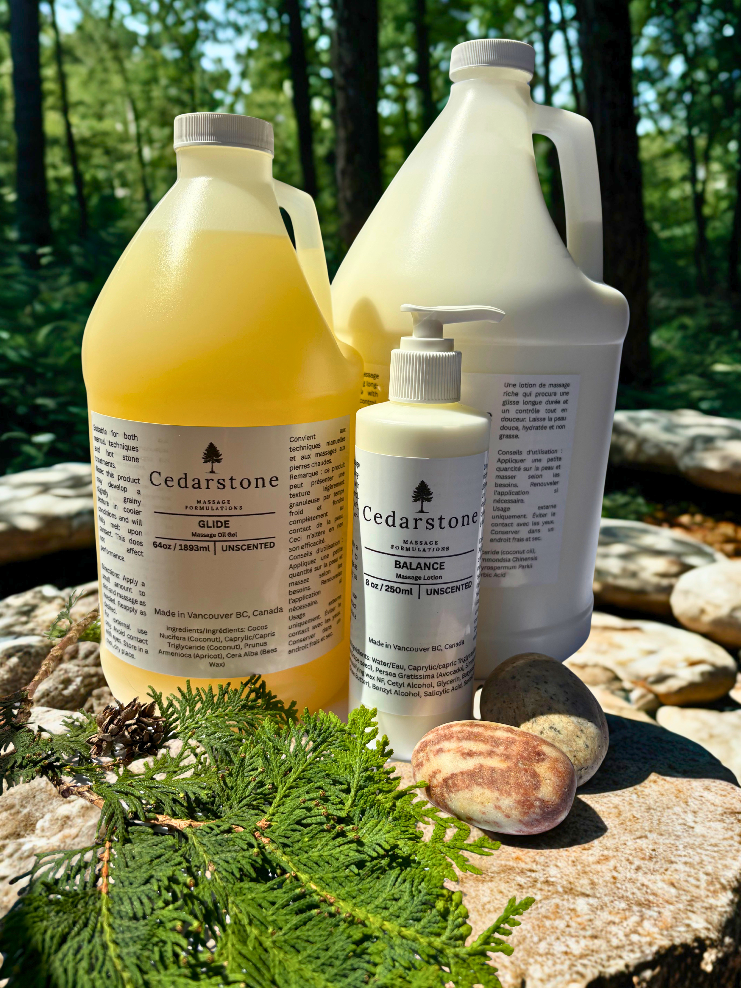 Three bottles of Cedarstone massage products placed on a natural surface with rocks and green foliage in the background.
